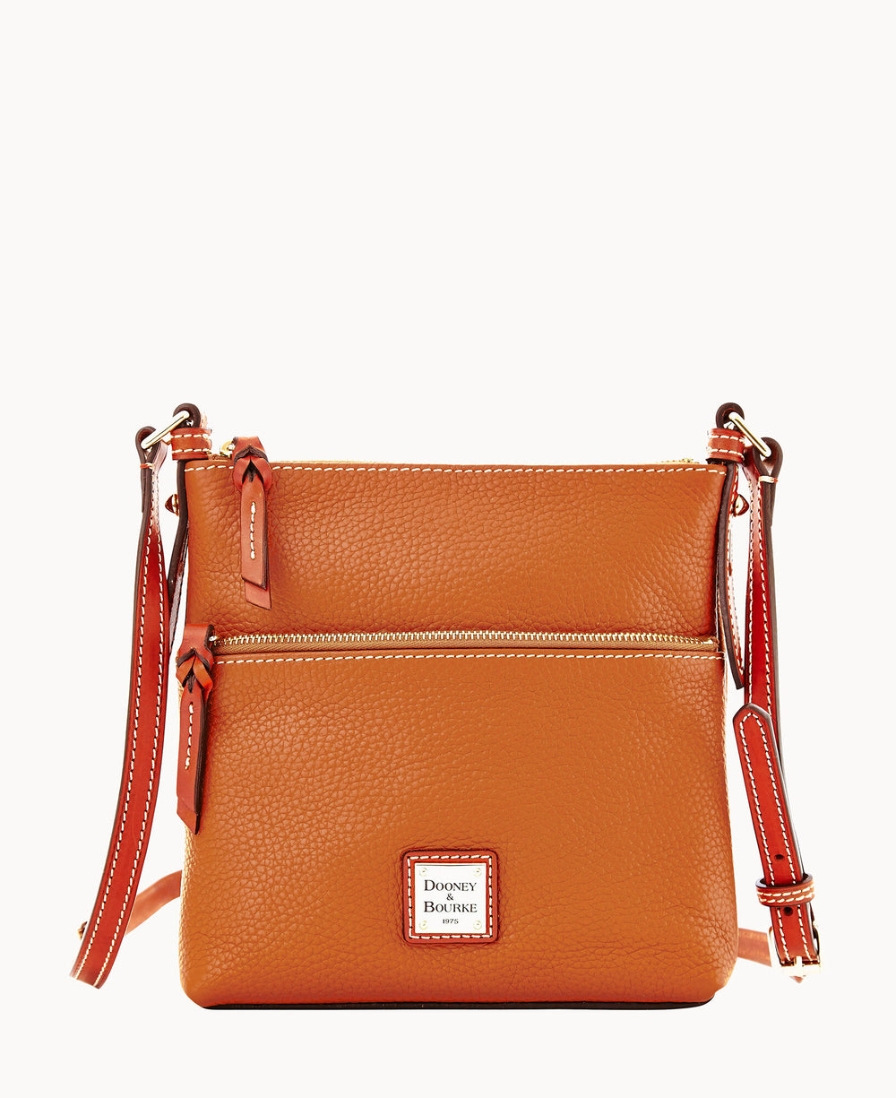 A small, textured, orange leather crossbody bag with a front zip pocket, adjustable strap, and a Dooney & Bourke logo patch at the bottom center.