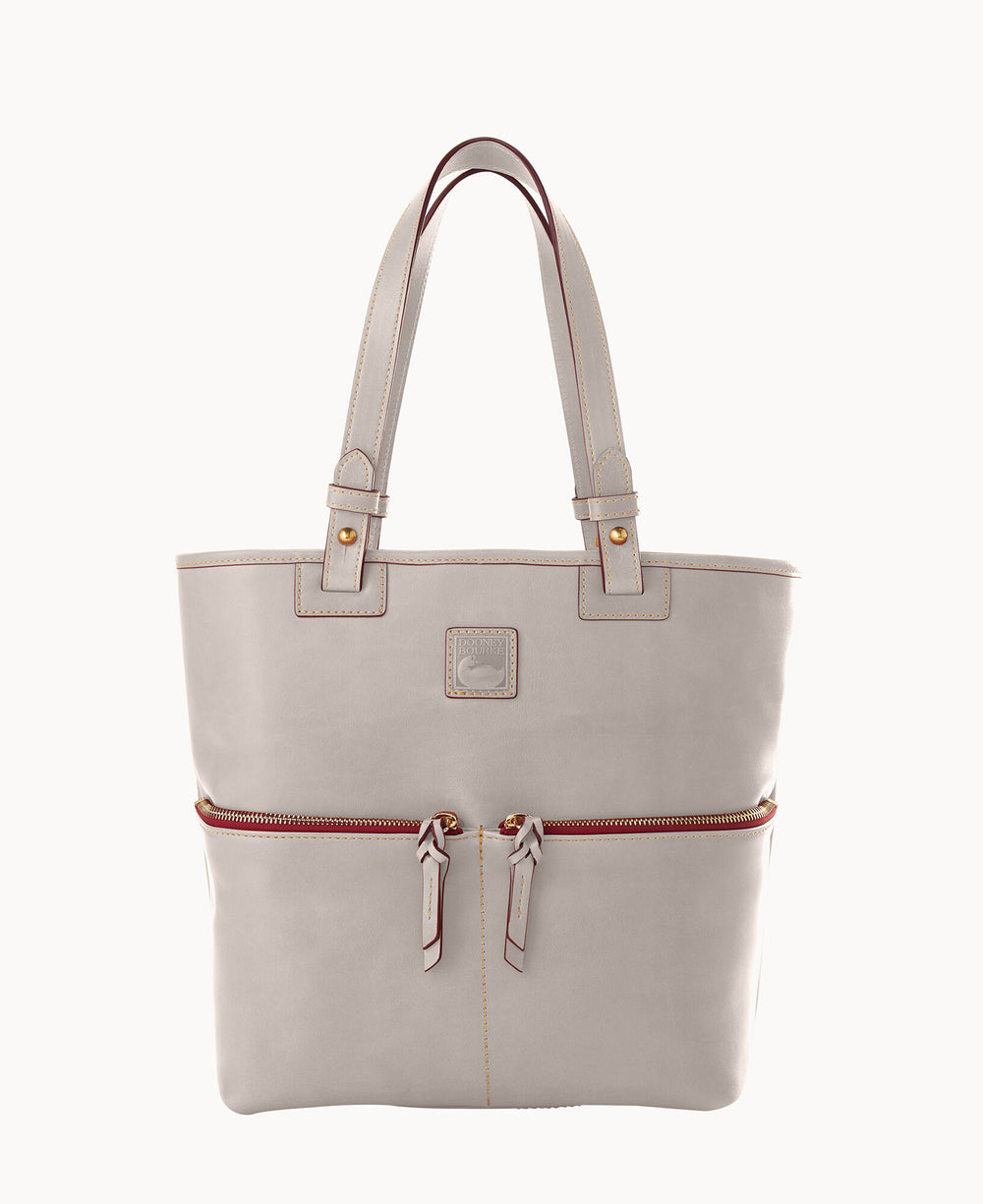 A light beige leather tote bag with double handles, gold hardware, a front zipper pocket with two zipper pulls, and subtle stitching details.
