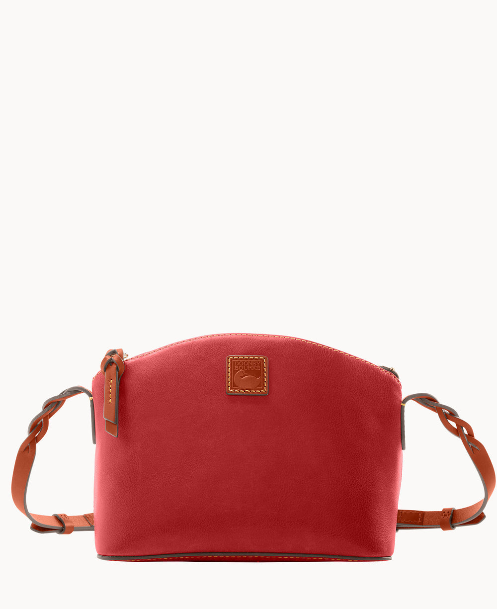 A red leather crossbody bag with a curved top, brown braided leather strap, and a small square leather logo patch on the front center.