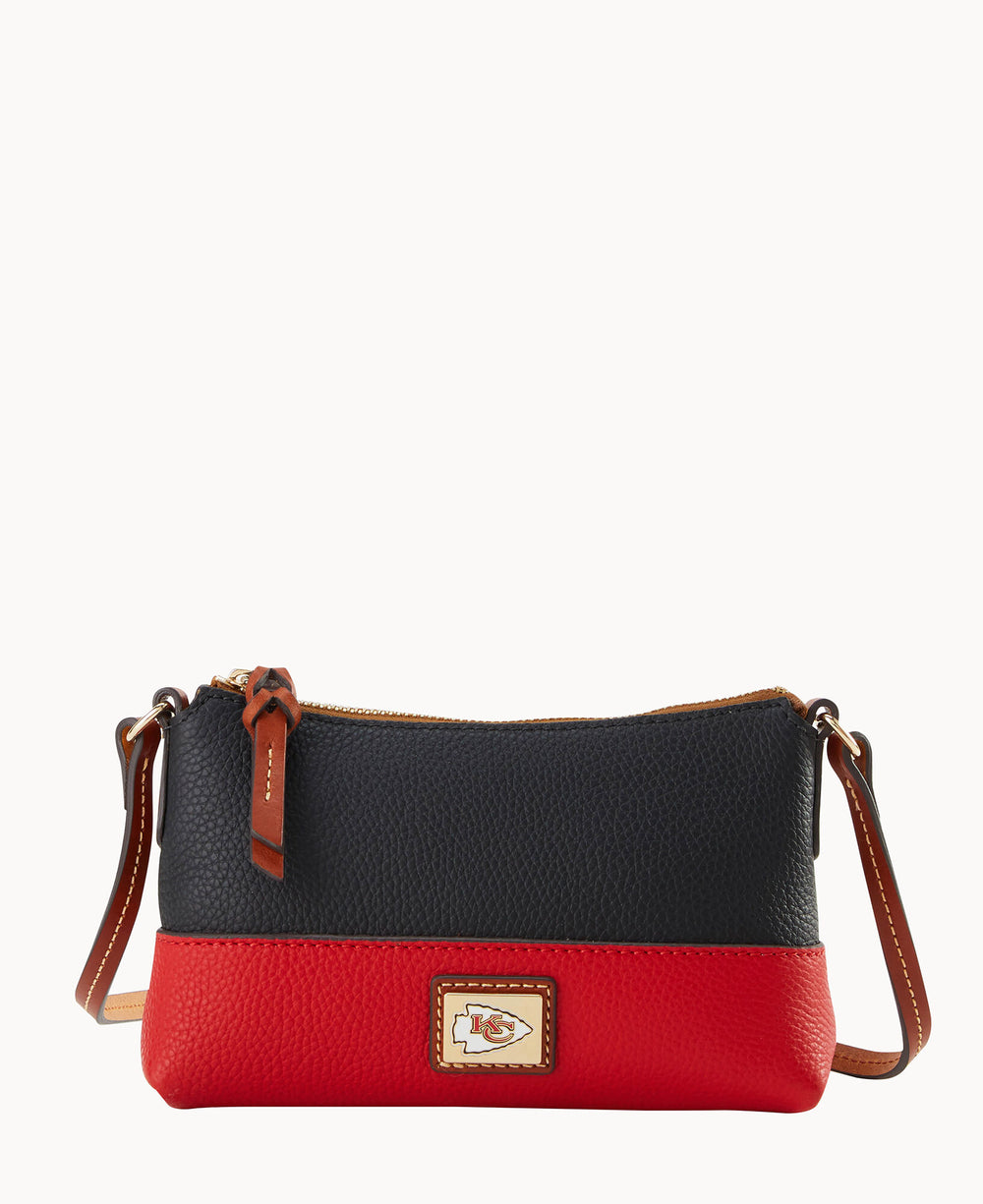 A small crossbody bag with a black upper section and red bottom, featuring a brown leather strap and zipper. The front has a rectangular patch displaying the Kansas City Chiefs logo.