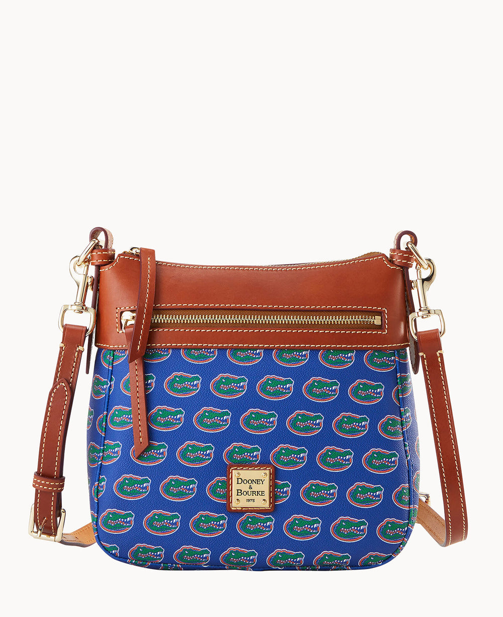 A blue crossbody bag with brown leather trim, gold hardware, a front zipper pocket, and an all-over University of Florida Gators logo pattern. The bag features a Dooney & Bourke label on the front.