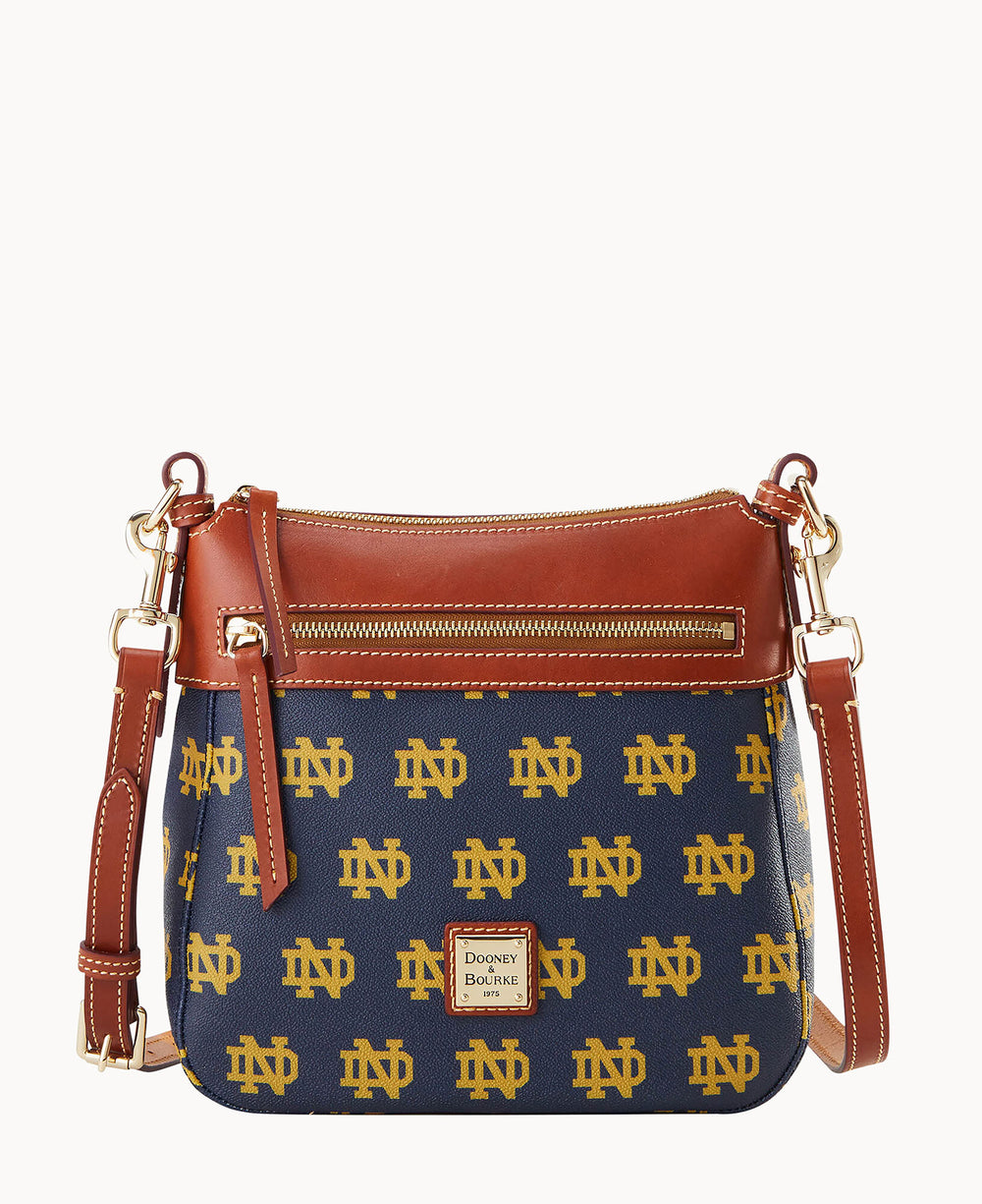 A navy blue Dooney & Bourke crossbody bag featuring repeating gold ND logos, brown leather trim, a front zipper pocket, and an adjustable strap with gold-tone hardware.