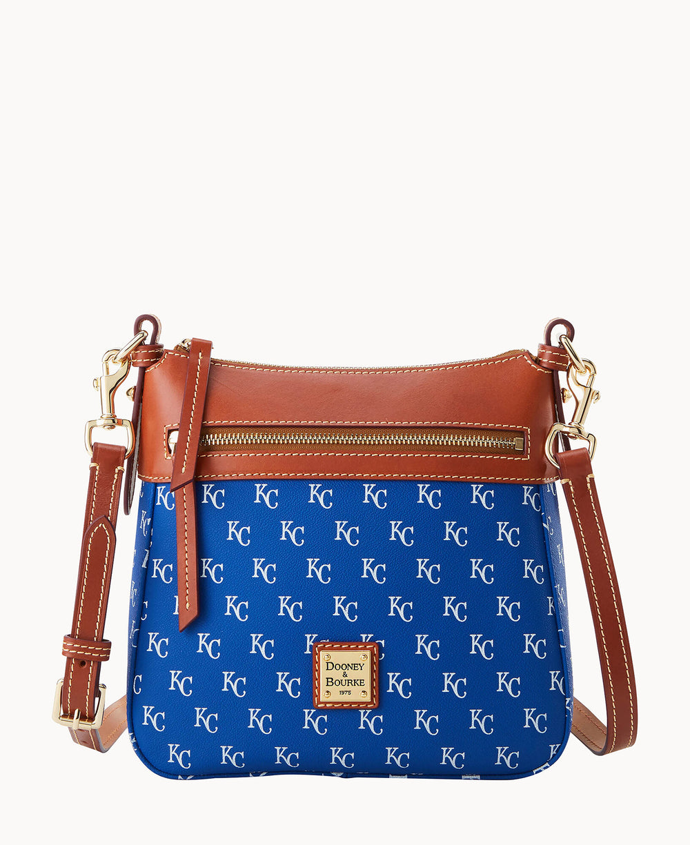 A blue crossbody bag with brown leather trim and gold hardware, featuring an all-over repeating KC pattern and a front zip pocket. The bag has a Dooney & Bourke logo plaque on the front.