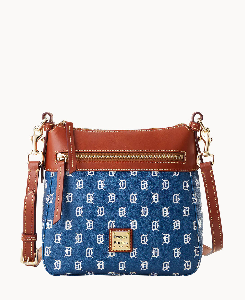 A blue Dooney & Bourke crossbody bag with brown leather trim, gold hardware, and a repeating white Detroit Tigers D logo pattern, featuring a front zipper pocket and adjustable strap.