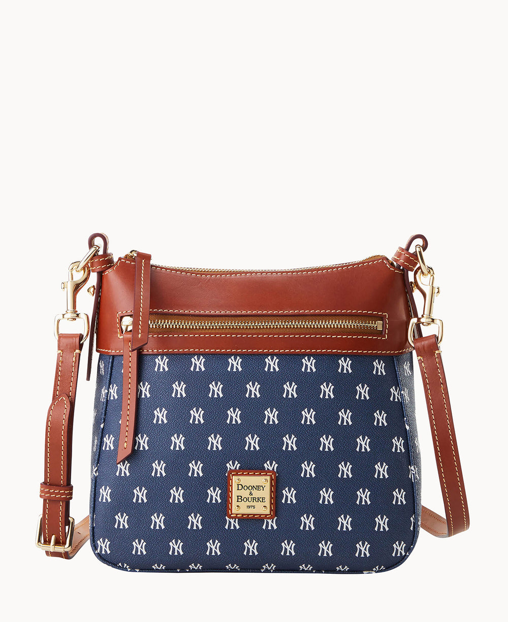 A navy blue crossbody bag with brown leather trim, gold hardware, and an adjustable strap. The bag features an all-over white New York Yankees logo print and a front zipper pocket.