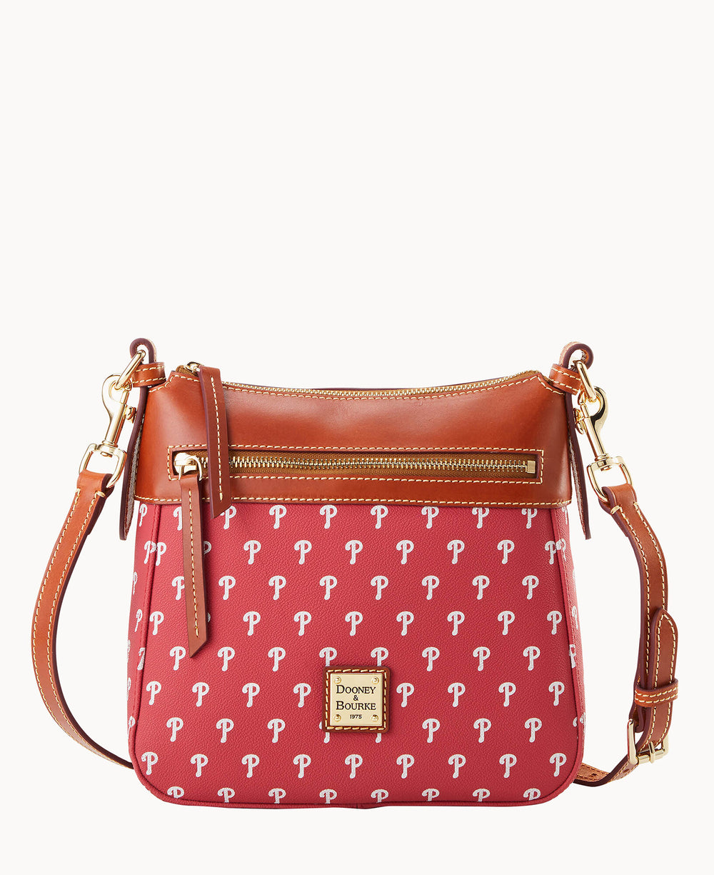 A red Dooney & Bourke crossbody bag featuring a repeating white letter P pattern, tan leather trim, a front zipper pocket, gold hardware, and an adjustable strap.