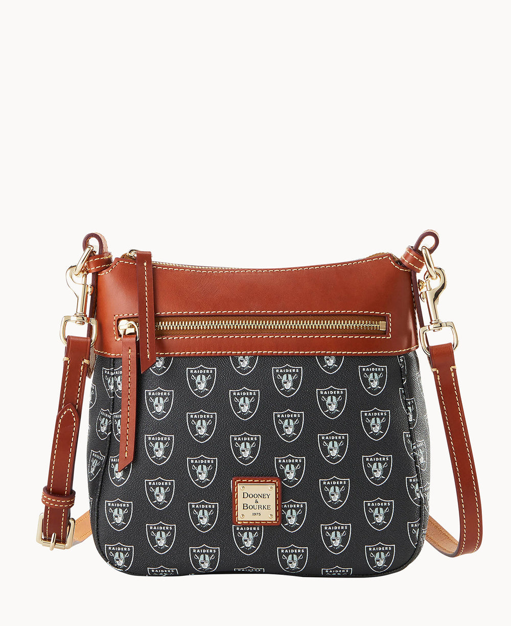A black crossbody bag with brown leather trim, gold hardware, a front zipper pocket, and an adjustable strap. The bag features a repeating white Las Vegas Raiders logo pattern and a Dooney & Bourke label.