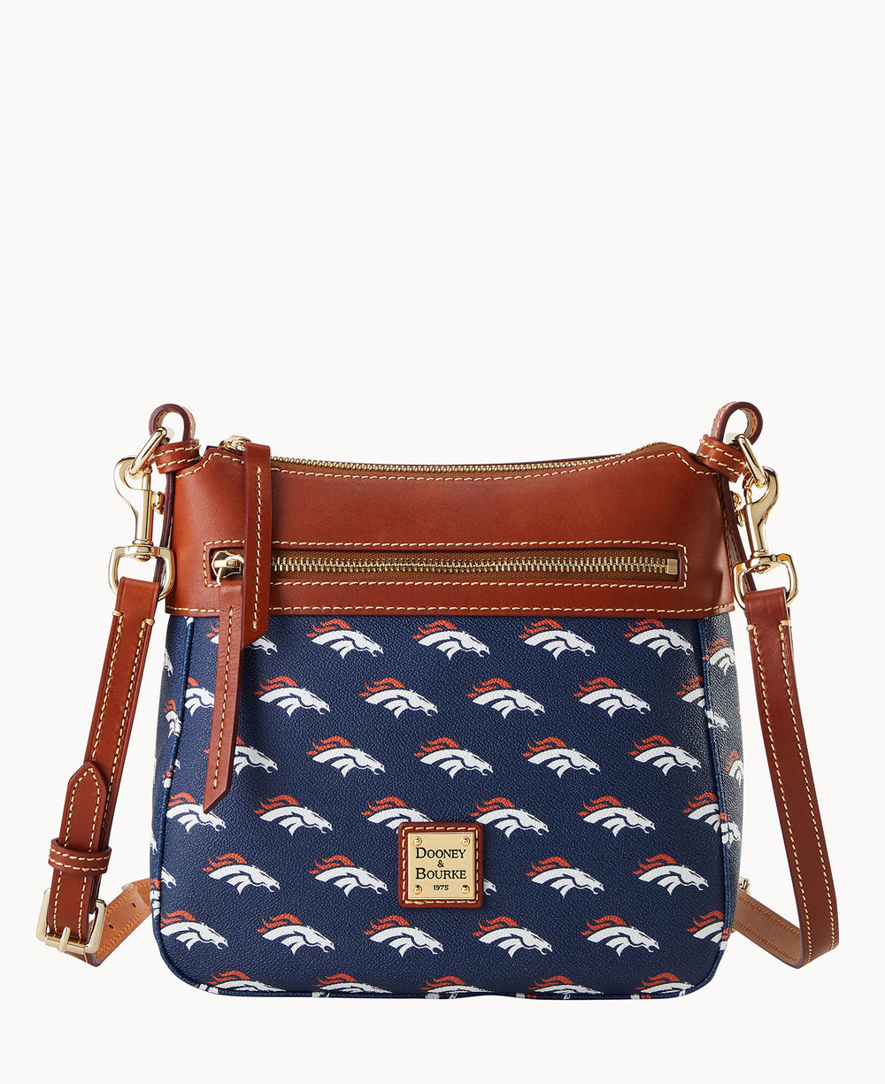 A navy blue crossbody bag with brown leather trim, gold hardware, and an all-over white and orange Denver Broncos logo pattern. The bag has a zippered front pocket and an adjustable strap.