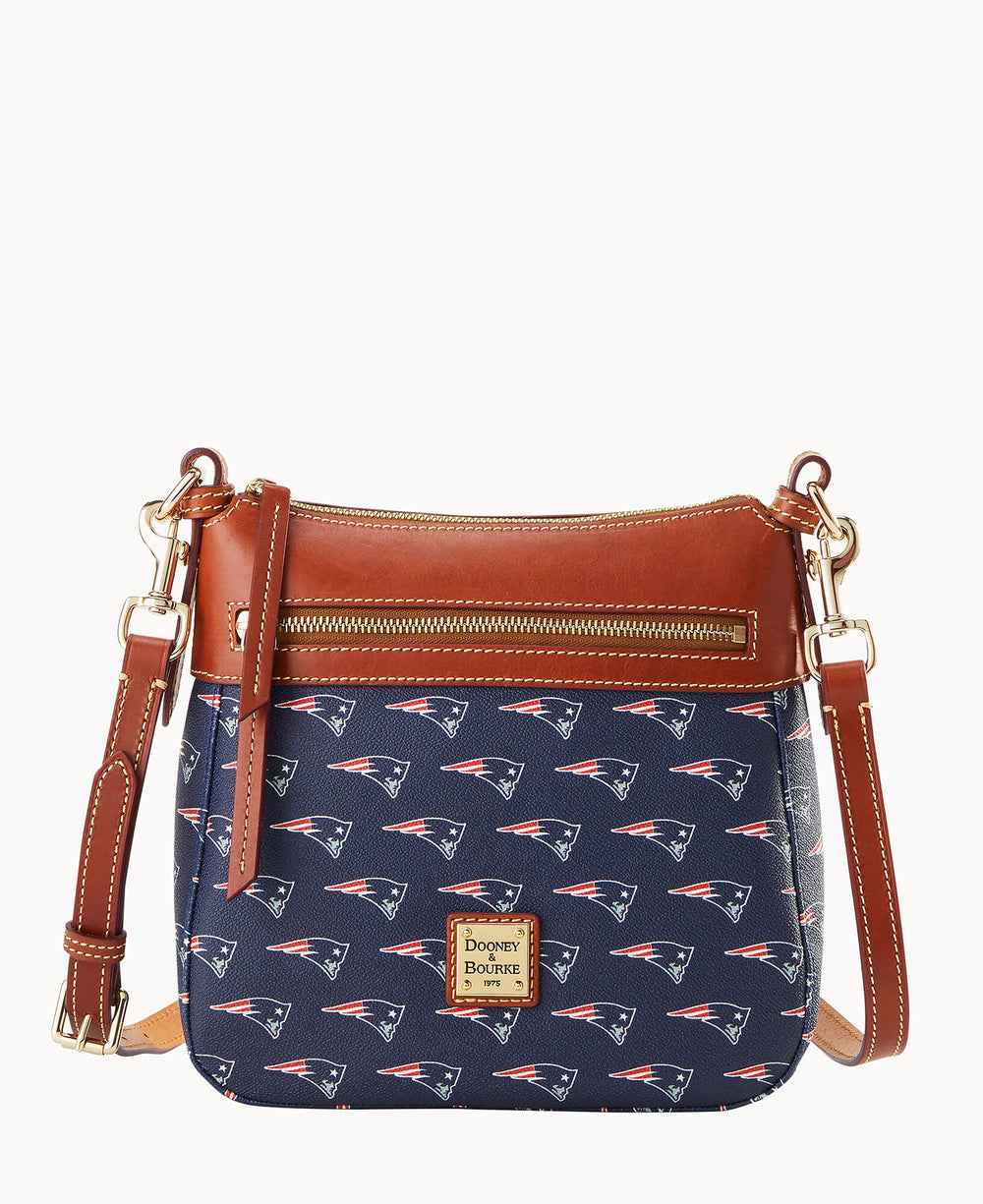 A small crossbody handbag with brown leather trim and strap, a front zipper pocket, and a navy blue body featuring a repeating New England Patriots logo pattern and a Dooney & Bourke logo patch.