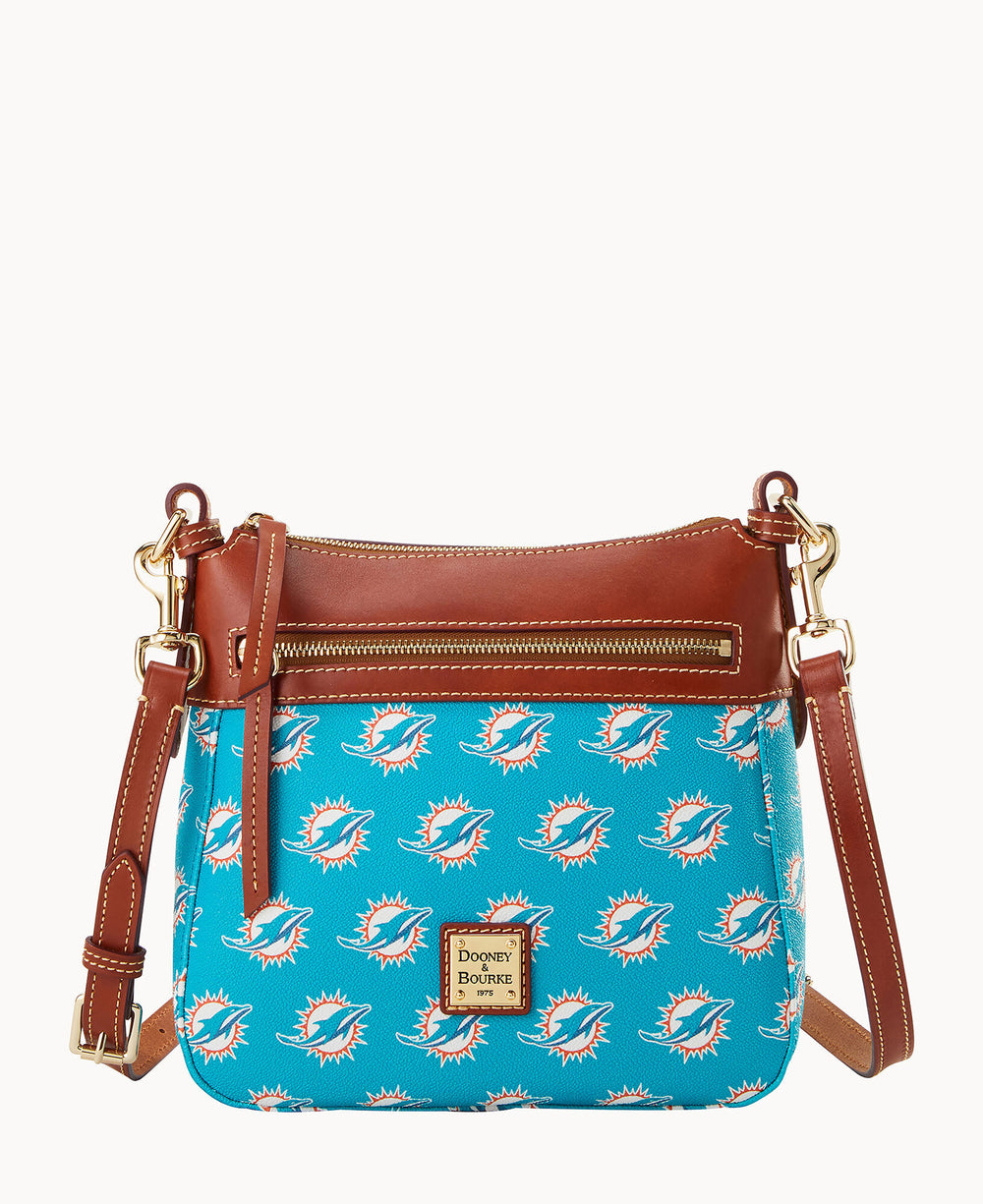 A turquoise crossbody bag with a brown leather trim and gold hardware, featuring a repeating Miami Dolphins logo pattern and a front zip pocket. The Dooney & Bourke logo is on a leather patch in front.