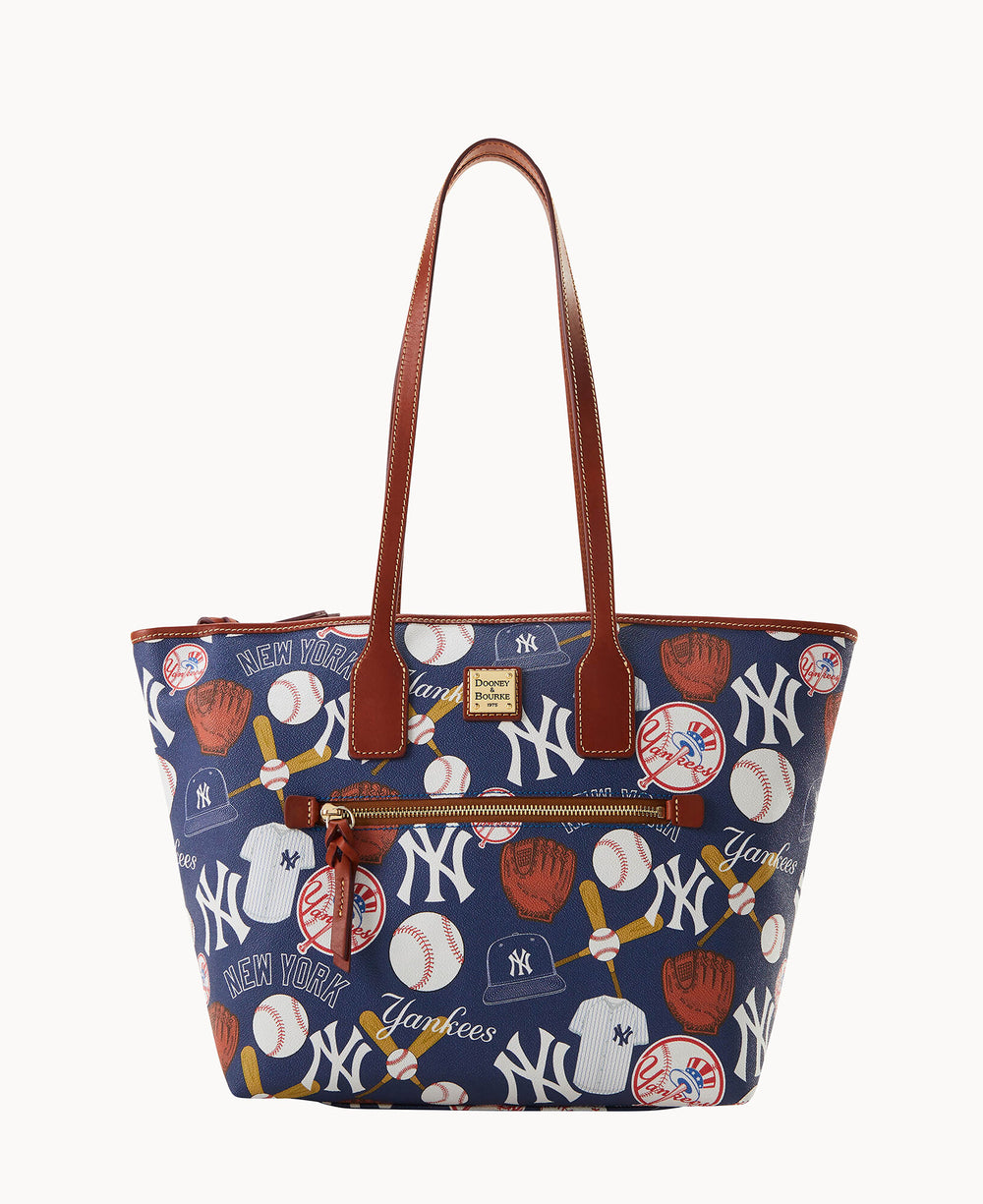 A navy tote bag with brown leather straps and trim, featuring a New York Yankees baseball-themed print with logos, baseballs, gloves, bats, and Yankees text in white and red.