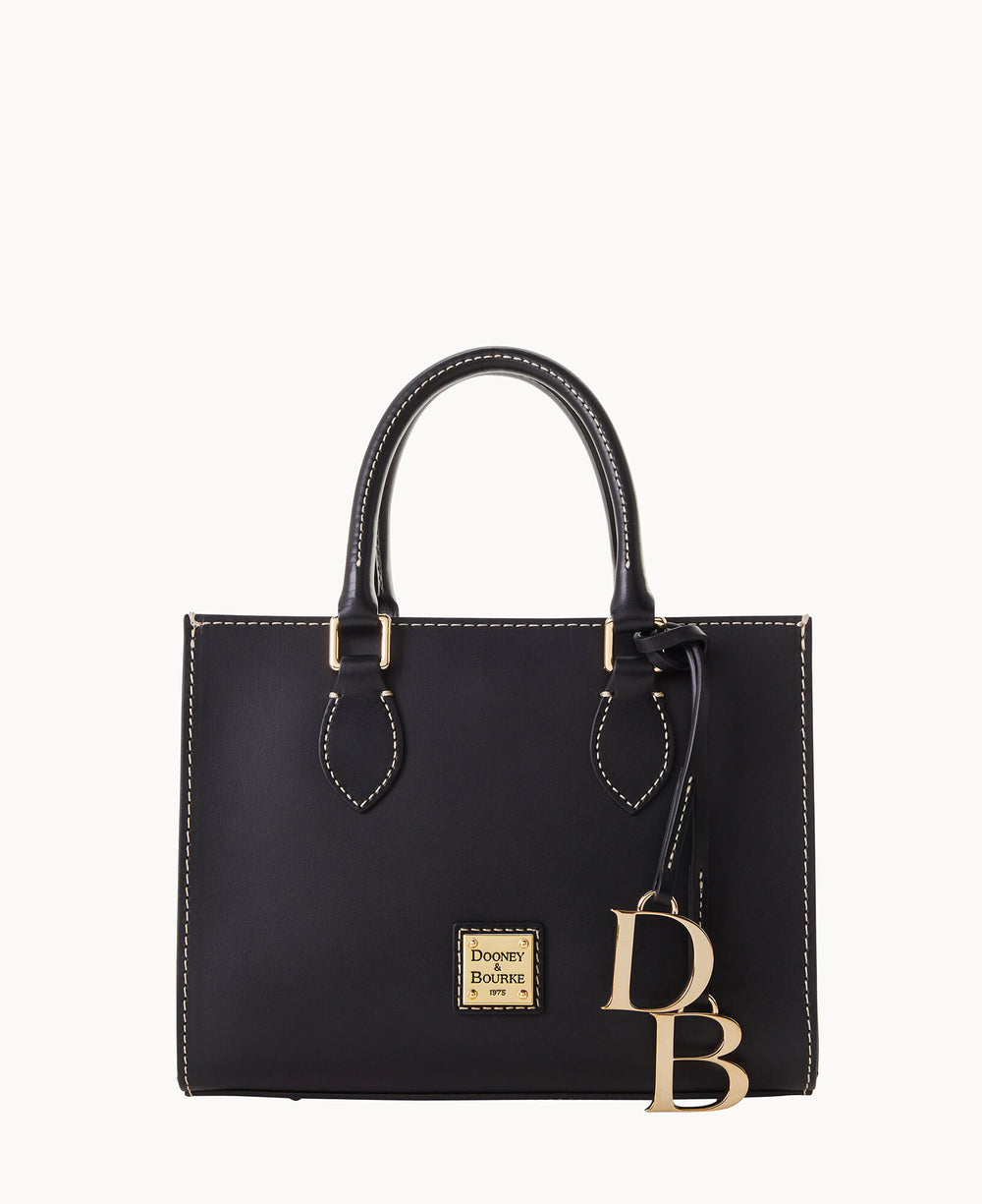 A black leather handbag with white stitching, two handles, a gold Dooney & Bourke logo plate on the front, and large gold DB charms hanging from one handle.