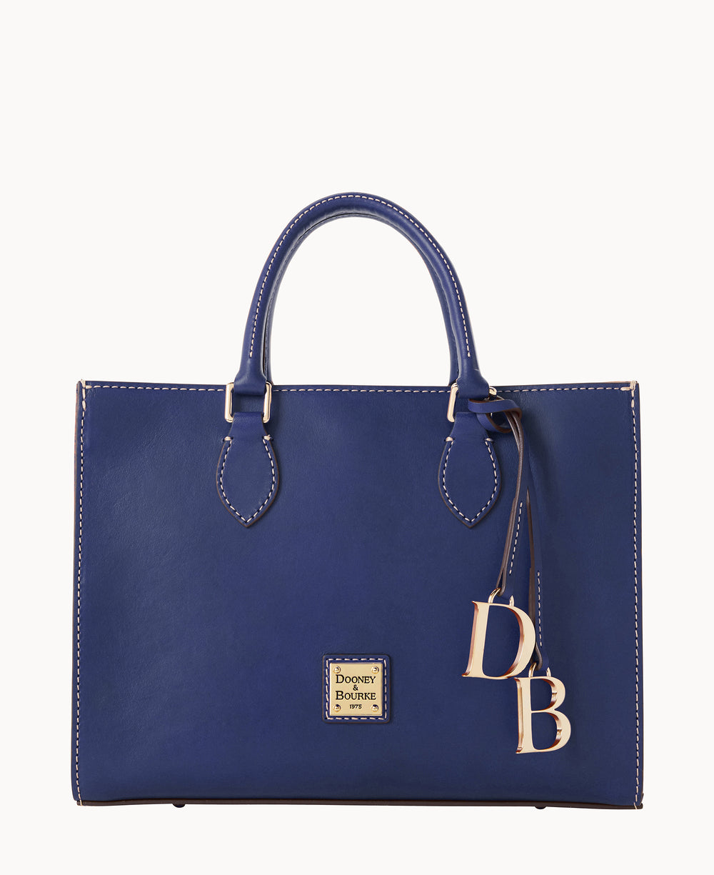 A structured, deep blue leather handbag with top handles, white stitching, a gold Dooney & Bourke logo plate on the front, and gold DB letter charms hanging from one handle.