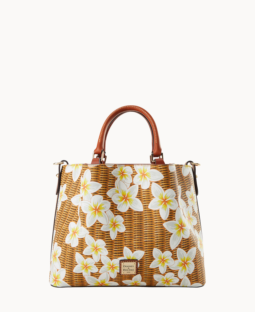 A structured handbag with brown leather handles, a wicker-style pattern, and white and yellow plumeria flowers printed all over. The bag has a gold logo plate on the front and a summery, tropical design.