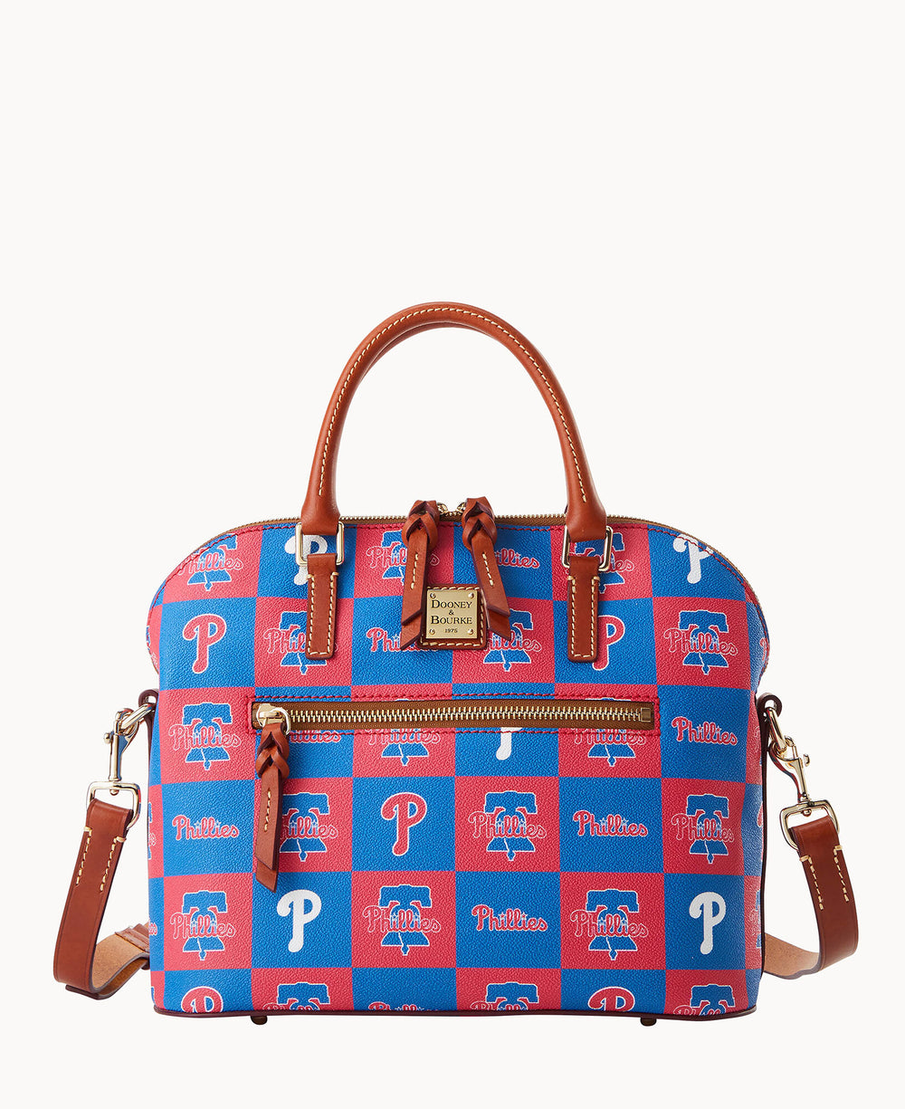 A handbag with brown leather handles and trim, decorated with a red and blue checkerboard pattern featuring various Philadelphia Phillies logos. It has a front zipper pocket and a detachable shoulder strap.