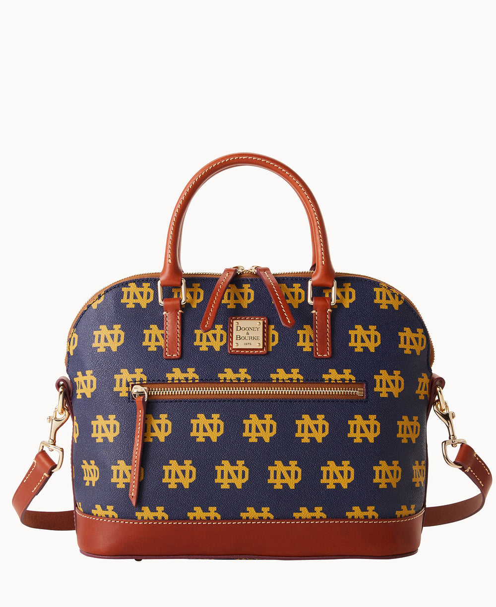 A dome-shaped handbag with brown leather handles and trim, featuring an all-over yellow ND Notre Dame logo pattern on a navy background and a front zip pocket.