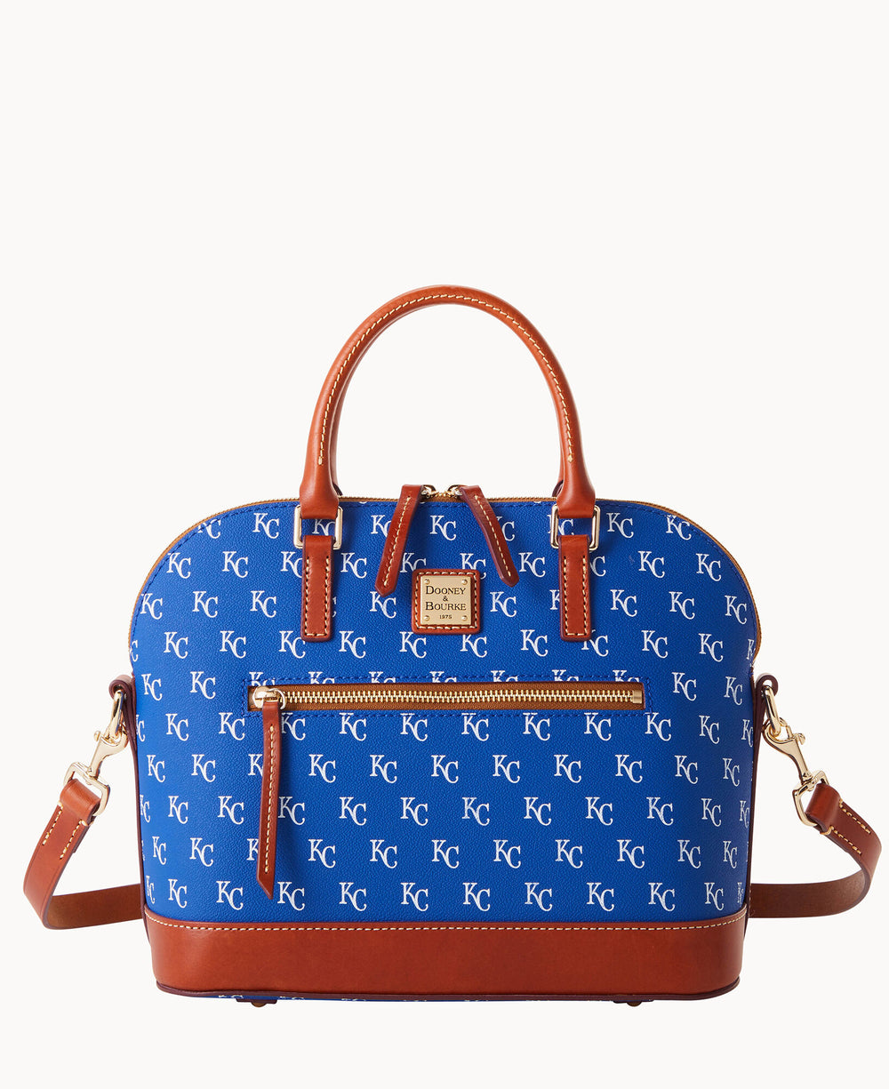 A blue handbag with brown leather handles and trim, featuring a repeating white KC pattern and a gold label on the front. The bag has a front zipper pocket and a detachable shoulder strap.