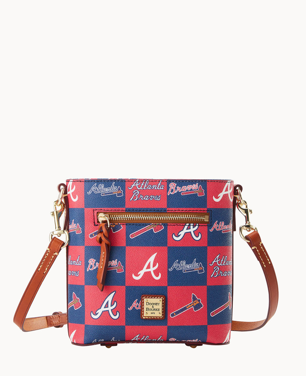 A red-and-blue crossbody purse featuring Atlanta Braves logos, tomahawks, and text. The bag has a brown leather strap, gold-tone hardware, a front zip pocket, and a Dooney & Bourke logo plaque on the bottom front.