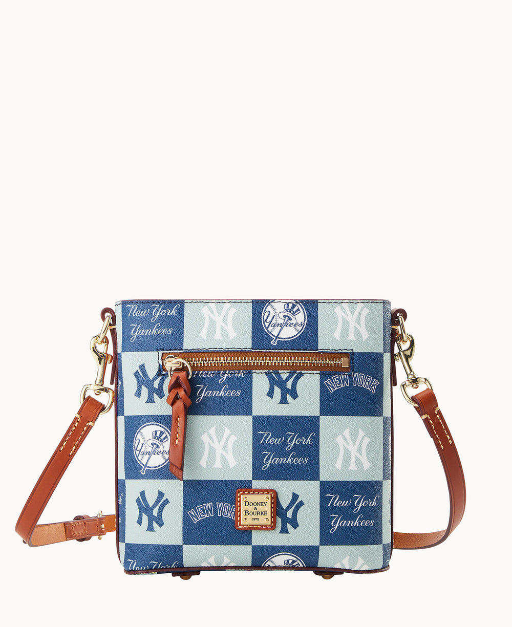 A small crossbody bag with adjustable brown leather straps, featuring a blue and white checkerboard pattern with various New York Yankees logos and New York Yankees text.