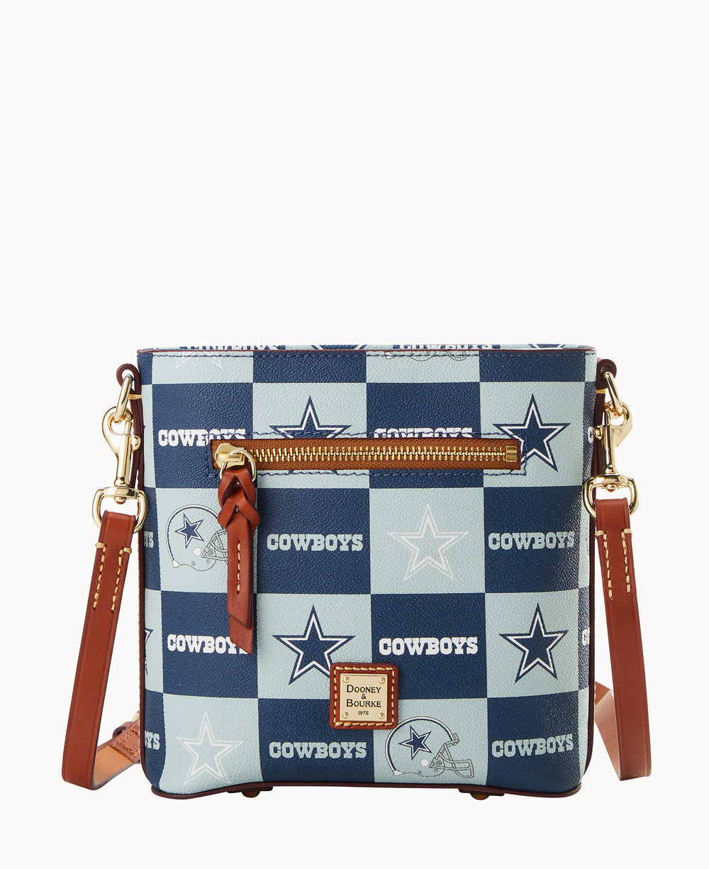 A crossbody bag with brown leather straps and a blue-and-white checkerboard pattern featuring the Dallas Cowboys logo, stars, and COWBOYS text. There is a front zipper pocket and a Dooney & Bourke logo patch.
