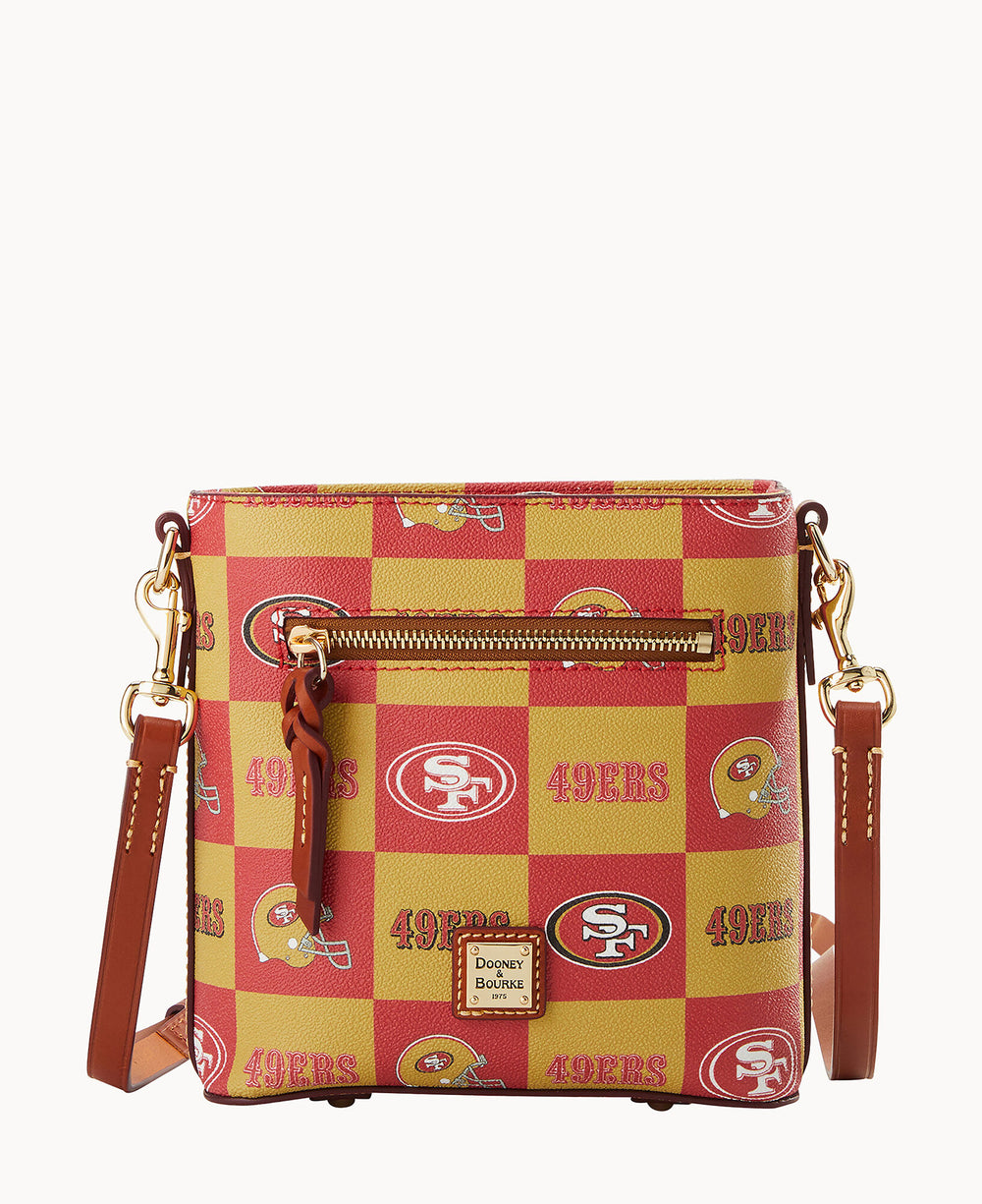 A crossbody bag with San Francisco 49ers logos and helmets in a red and gold checkerboard pattern, featuring a front zipper pocket, brown leather strap, and gold-tone hardware.