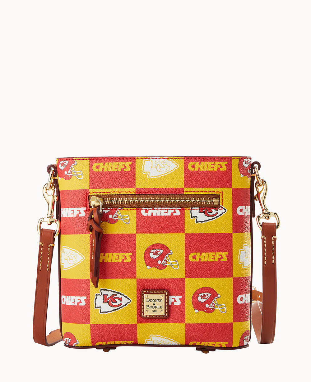 A square crossbody bag with a red and yellow checkered Kansas City Chiefs pattern, featuring team logos, helmets, and â€œCHIEFSâ€ text. The bag has a brown leather strap and gold hardware with a front zipper pocket.