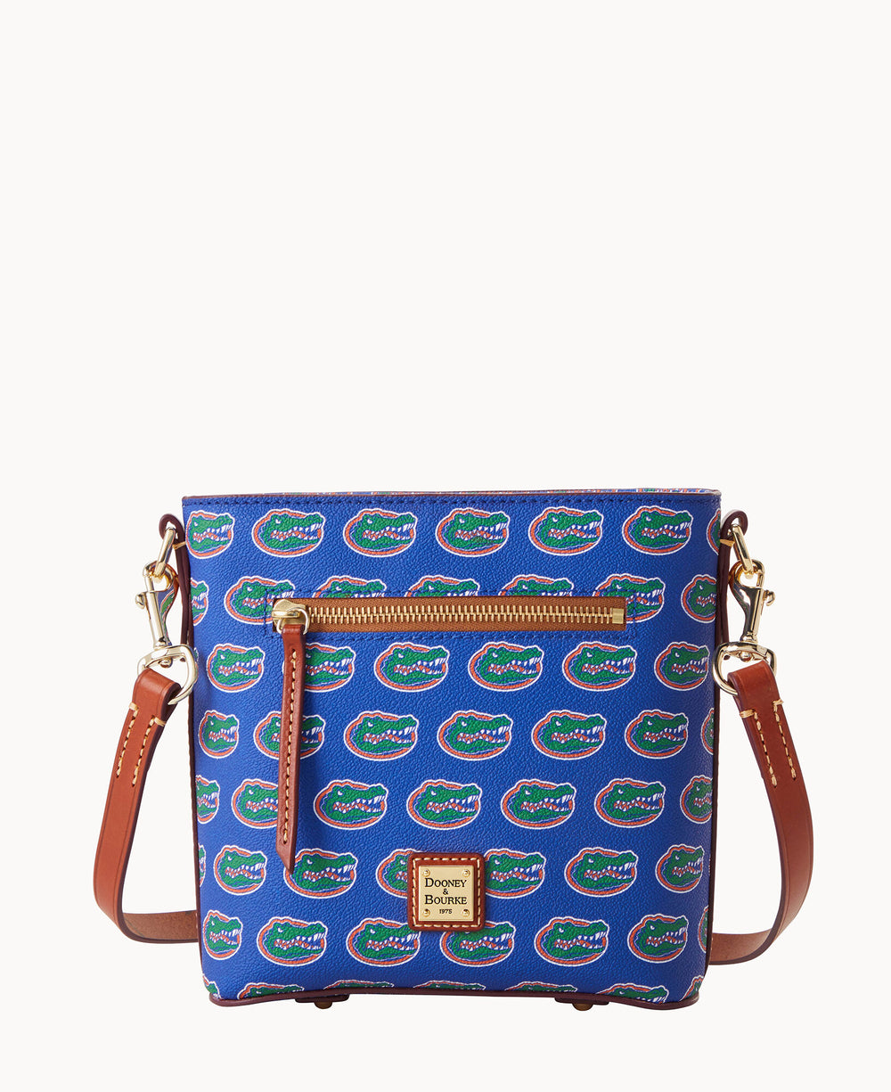 A blue crossbody bag with brown leather straps and accents, featuring a repeating University of Florida Gators logo pattern and a front zipper pocket.