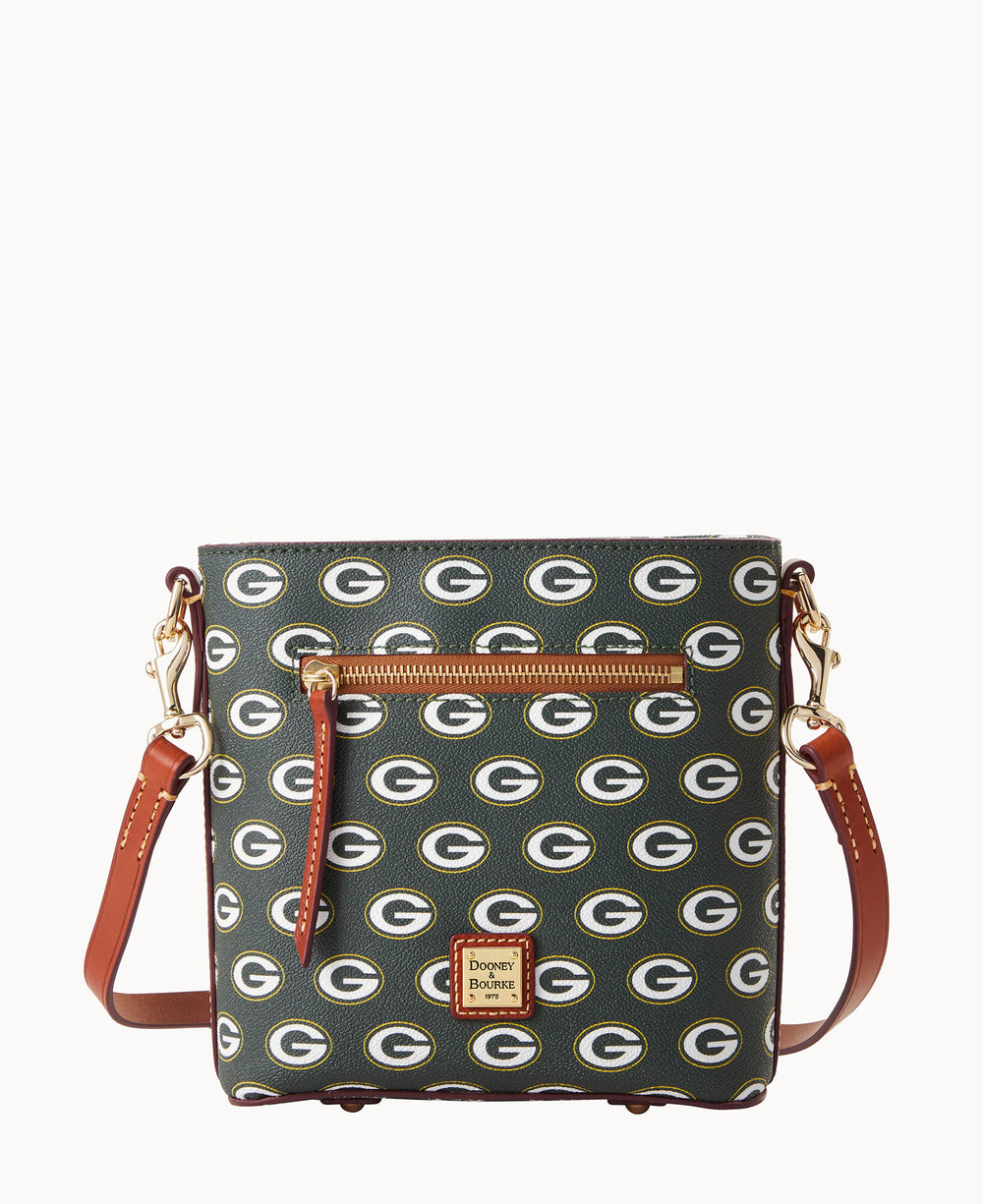 A green Dooney & Bourke crossbody bag featuring a repeating Green Bay Packers G logo pattern, a front zip pocket, gold hardware, and brown leather straps.