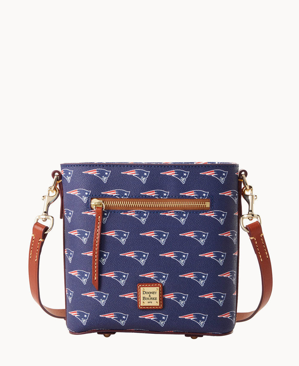 A navy blue crossbody bag with brown leather straps and a front zipper pocket, featuring a repeating New England Patriots logo pattern and a Dooney & Bourke logo patch on the front.