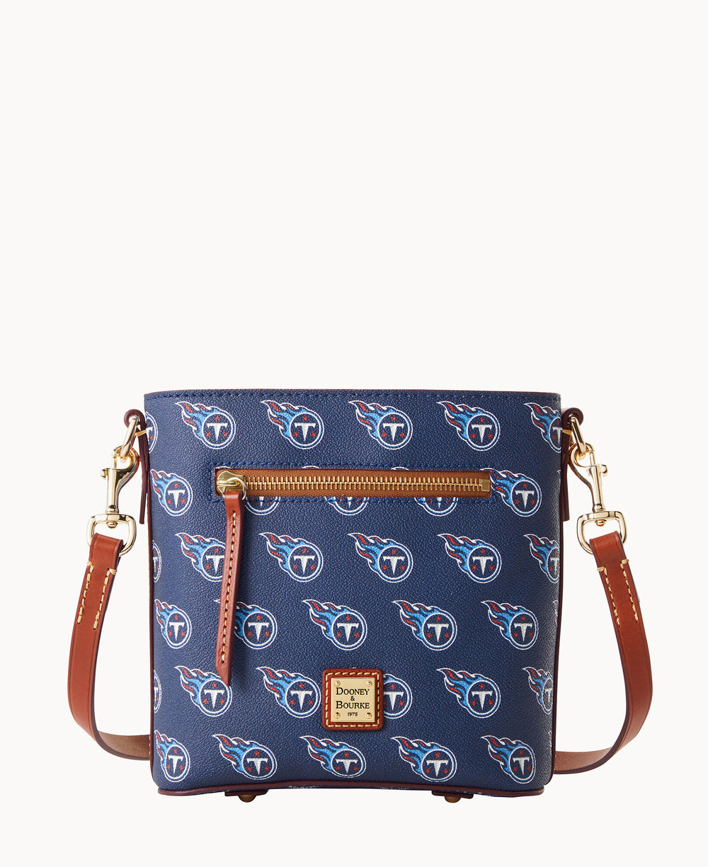A blue crossbody bag with brown straps, gold hardware, and a front zipper pocket, featuring repeating Tennessee Titans NFL team logos and the Dooney & Bourke logo patch on the front.