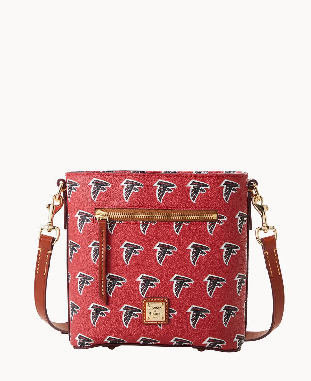 A red crossbody bag with brown leather straps, gold hardware, and an exterior zipper pocket. The bag features a repeating black and white Atlanta Falcons logo pattern and a Dooney & Bourke label on the front.