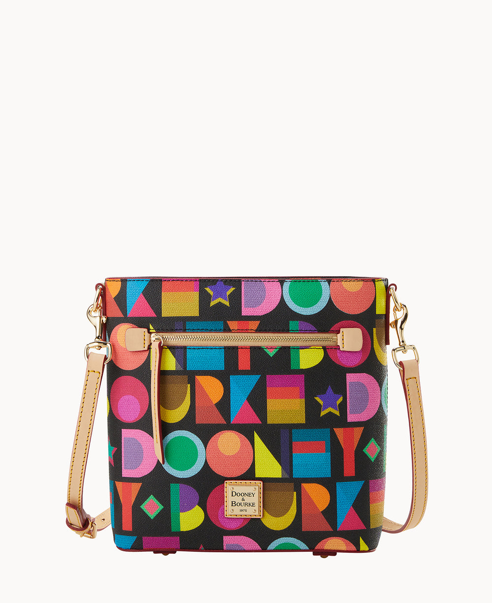 A square crossbody bag with a colorful, geometric pattern featuring letters in various fonts and sizes, gold hardware, a front zipper pocket, and a tan leather strap. The bag has a Dooney & Bourke label on the front.