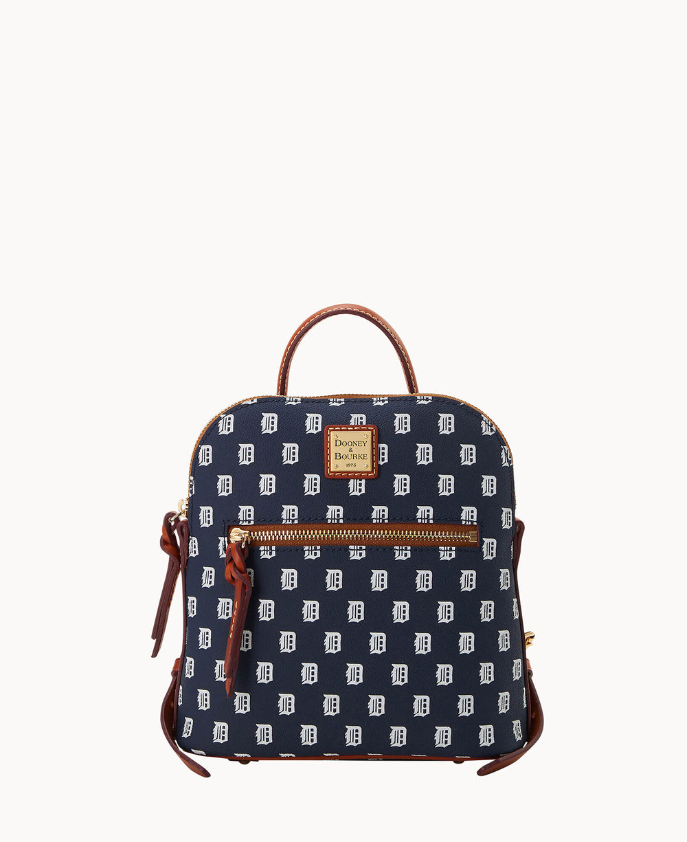 A navy blue mini backpack with brown leather accents, front zip pocket, and white repeating letter D pattern. The bag has a top handle and gold-tone hardware, featuring a Dooney & Bourke logo patch.