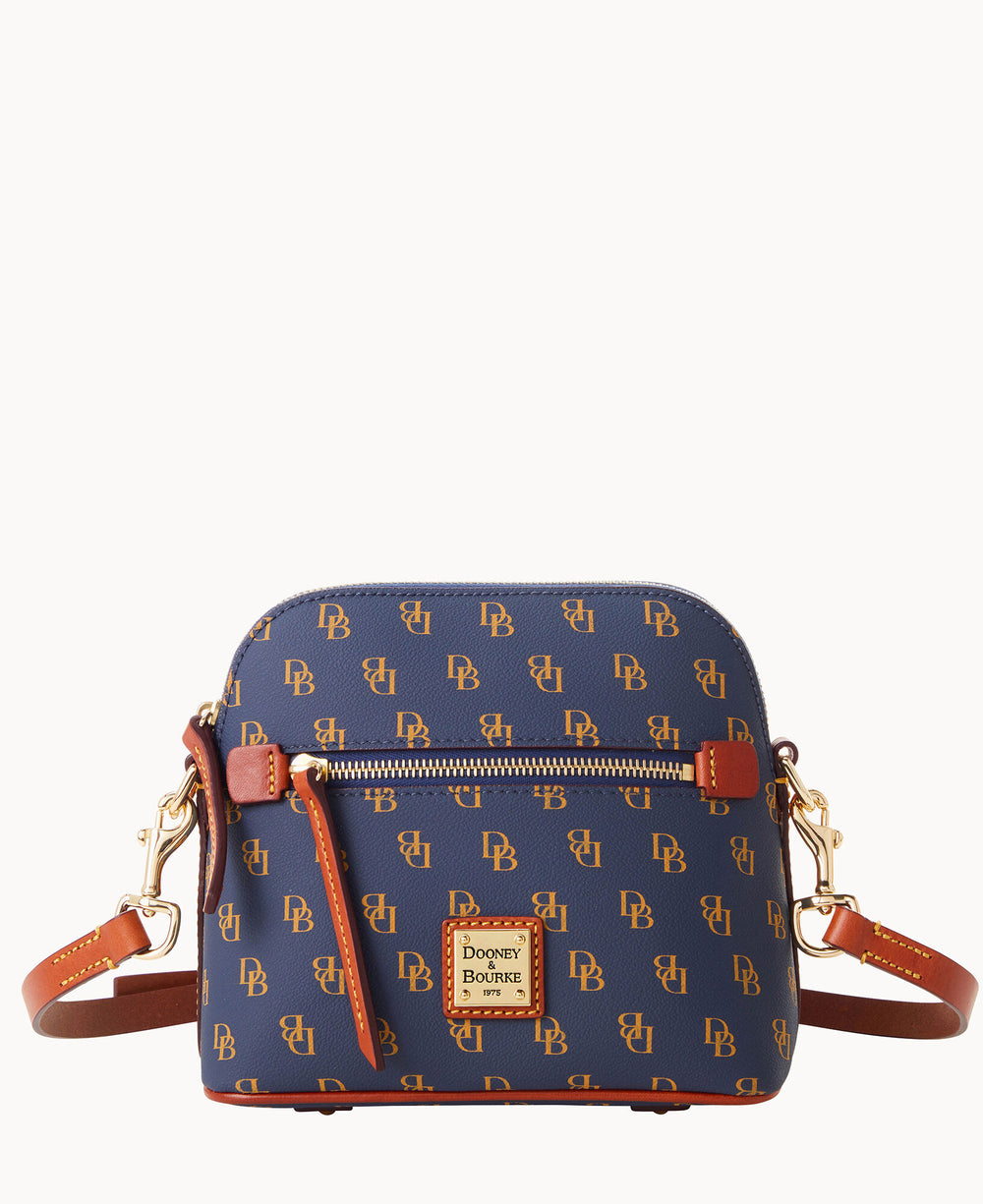 A small, navy blue Dooney & Bourke crossbody bag with a brown leather strap and trim, gold hardware, and a repeating DB logo pattern. A front zipper pocket and a logo patch are visible on the front.