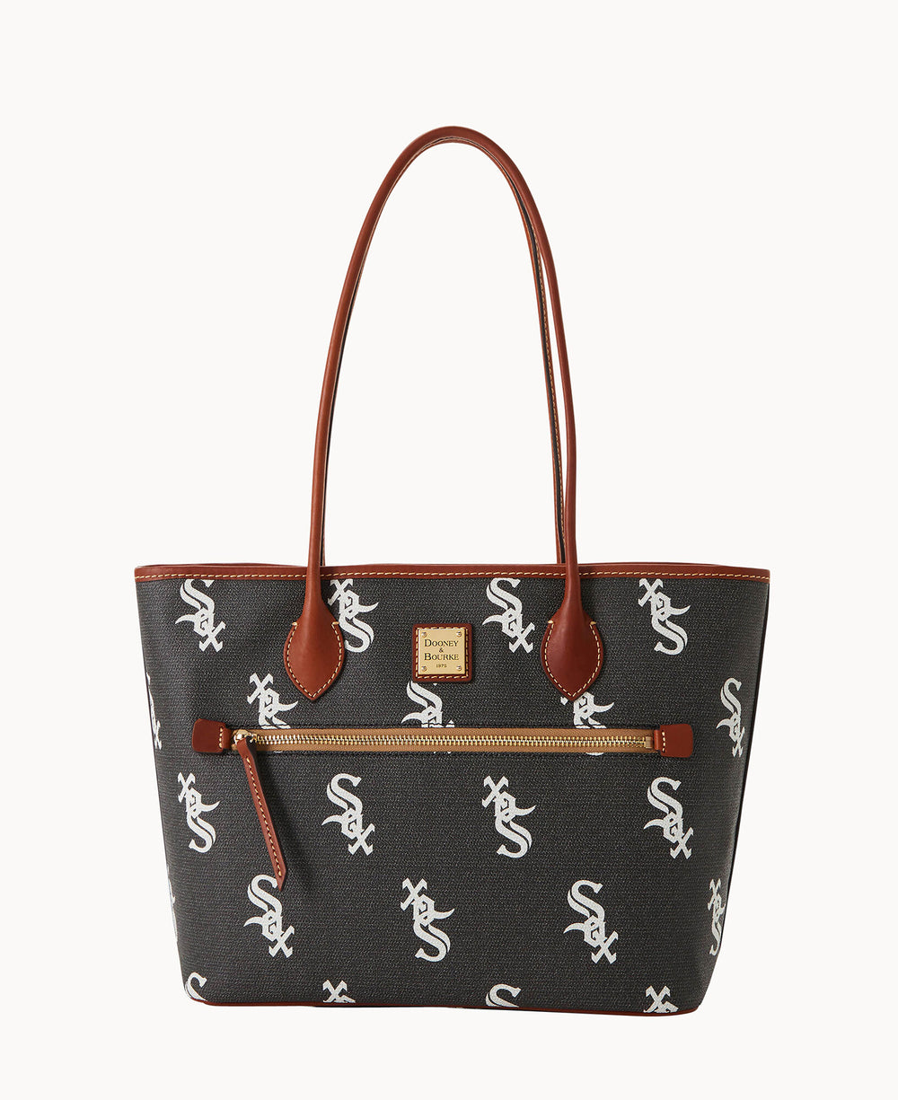 A black tote bag with brown leather handles and trim, featuring a white Sox logo pattern and a front zip pocket with a gold zipper.