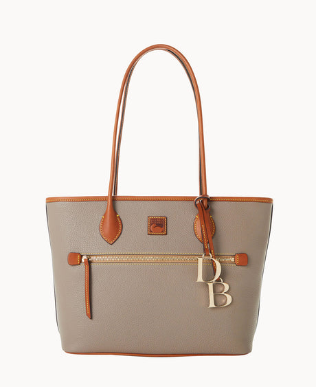 A taupe leather tote bag with brown trim, long handles, an exterior zip pocket, and gold-tone DB charms hanging from one handle.