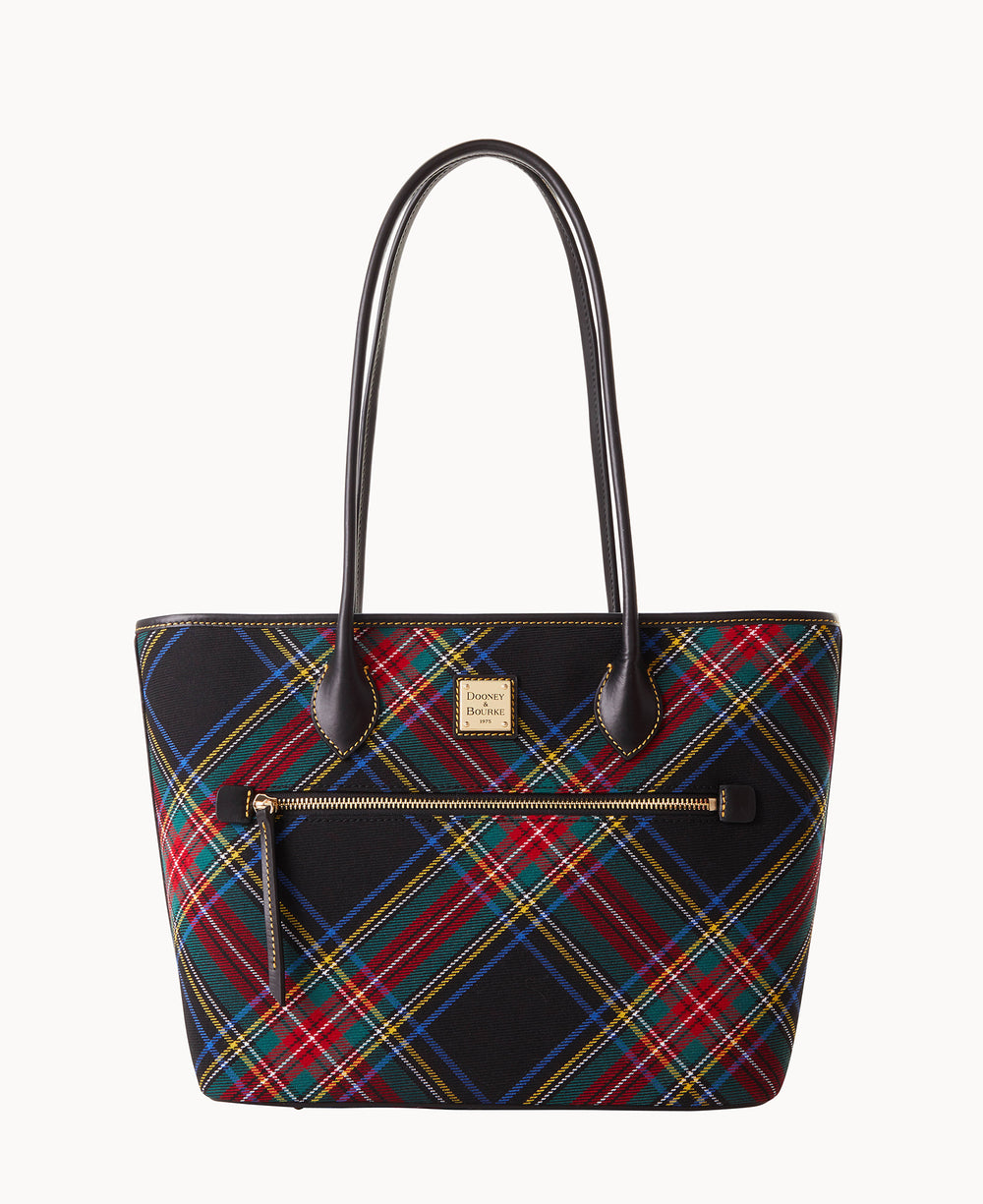 A tote bag with a red, green, blue, and yellow plaid pattern, black handles, a front zipper pocket, and a gold brand logo on the front. The background is white.