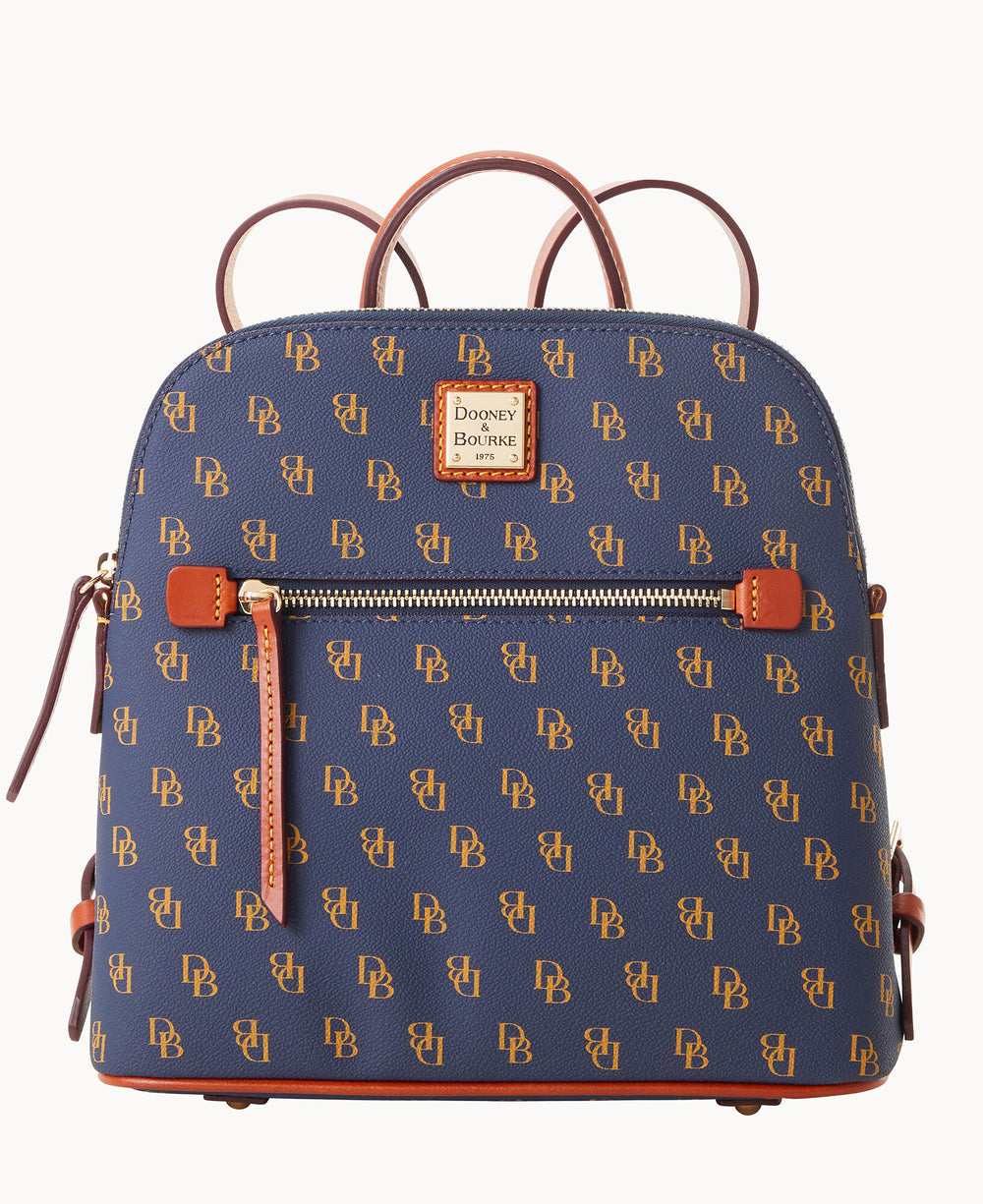 A navy blue Dooney & Bourke backpack with tan leather accents and a repeating gold DB logo pattern, featuring a front zipper pocket and a square brand label.