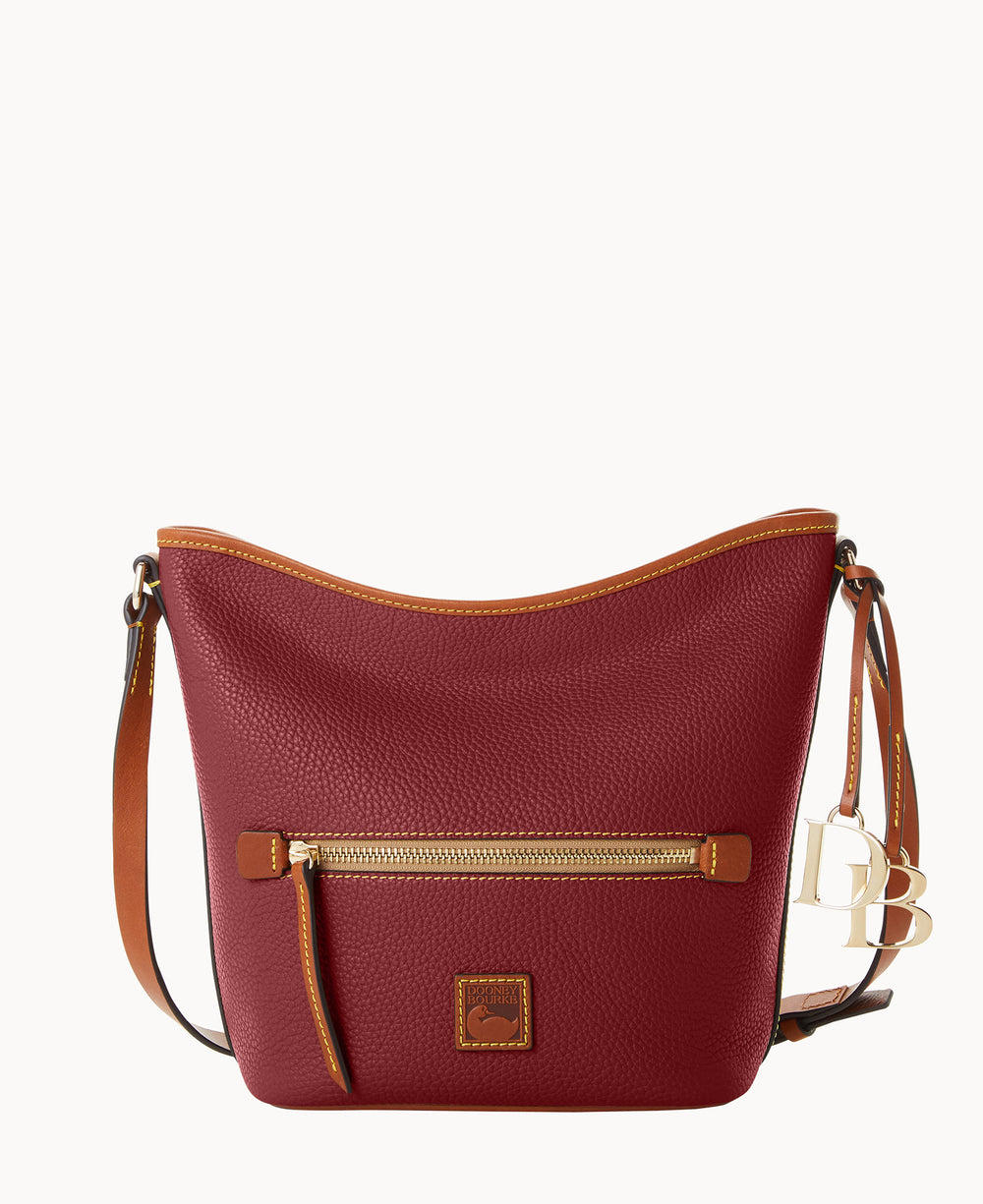 A red leather shoulder bag with a brown leather trim, a front zippered pocket, gold-tone hardware, and a brown adjustable strap. The bag also features a small logo patch and decorative letter charms.