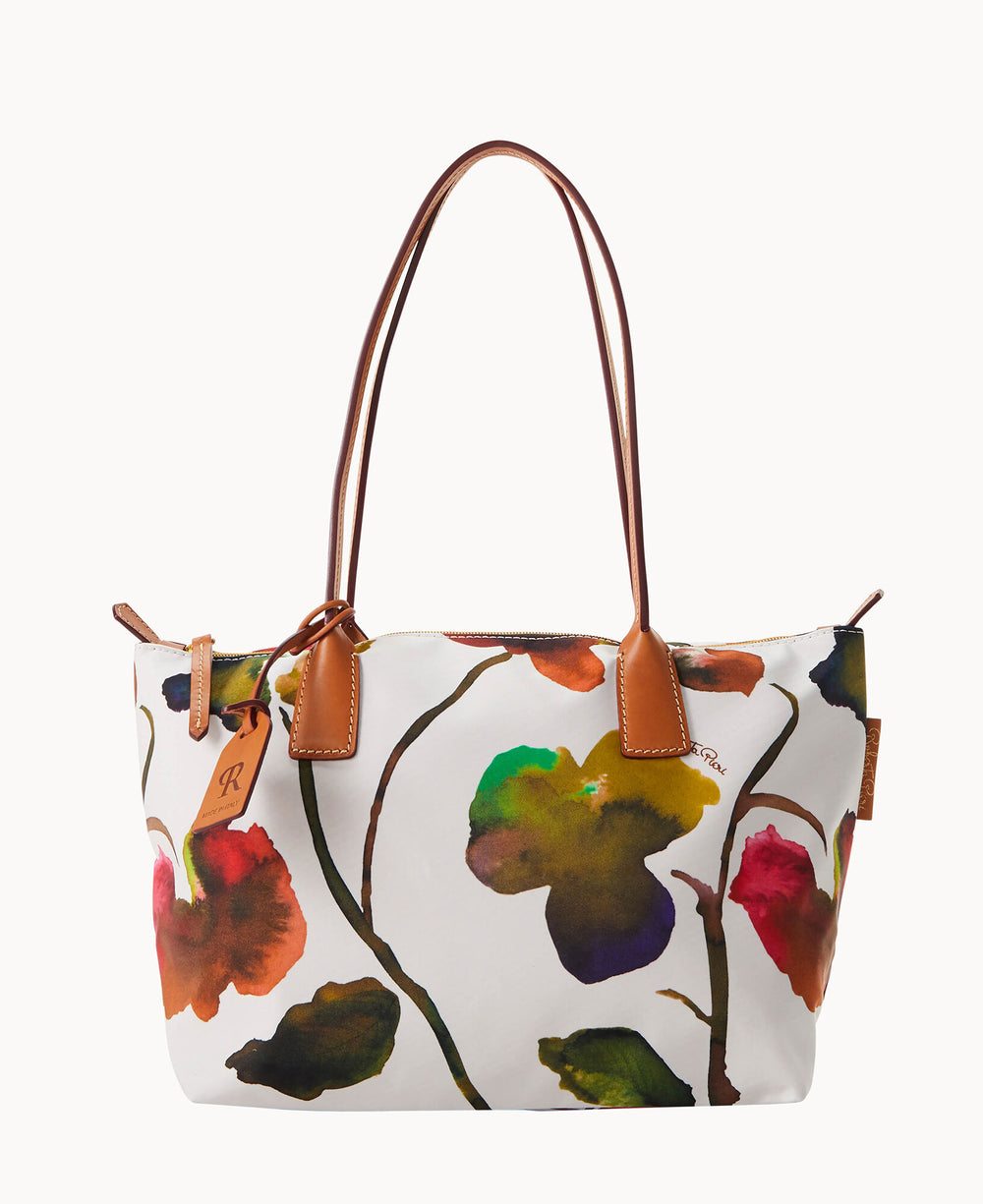 A medium-sized tote bag with leather handles and a white background featuring a colorful, abstract floral pattern in shades of green, orange, red, and yellow. A small brown tag hangs from one handle.