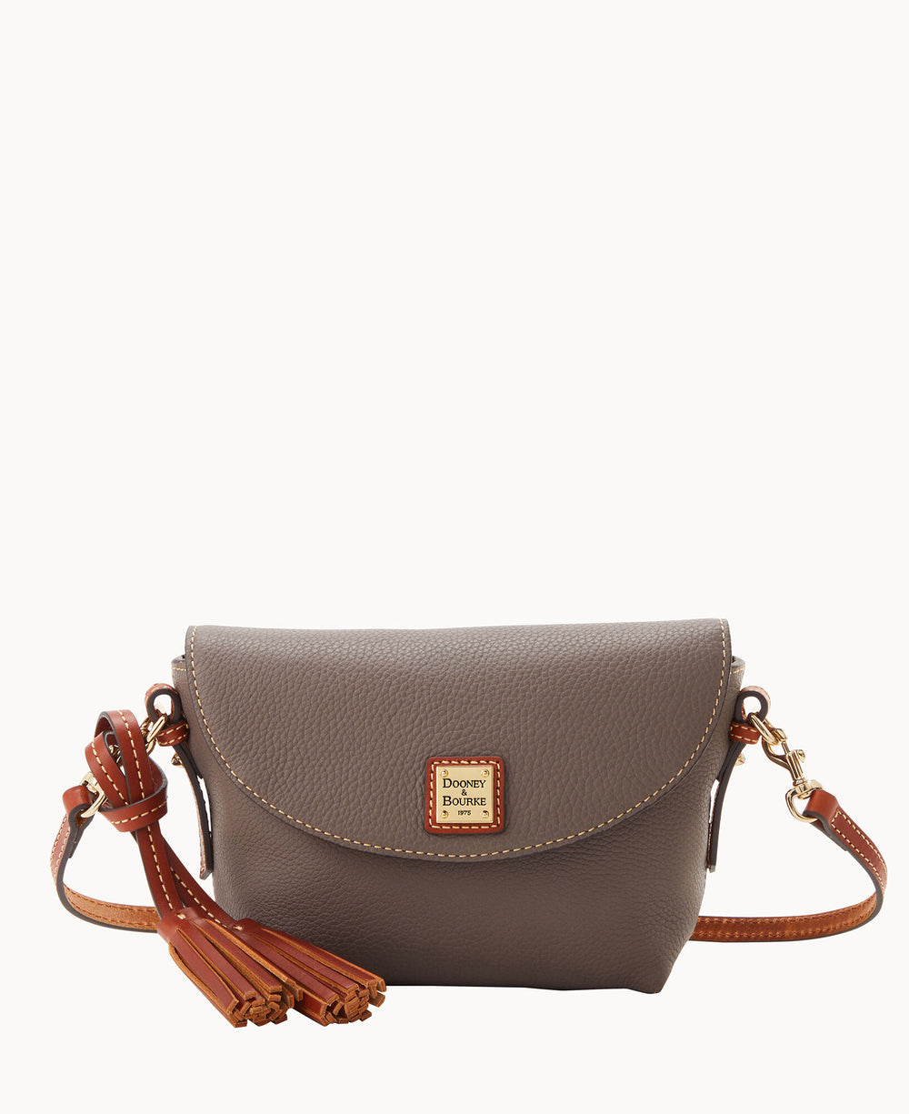 A small taupe leather crossbody bag with a flap closure, brown leather tassels, and an adjustable strap. The front features a gold and red Dooney & Bourke logo patch with stitched detailing.
