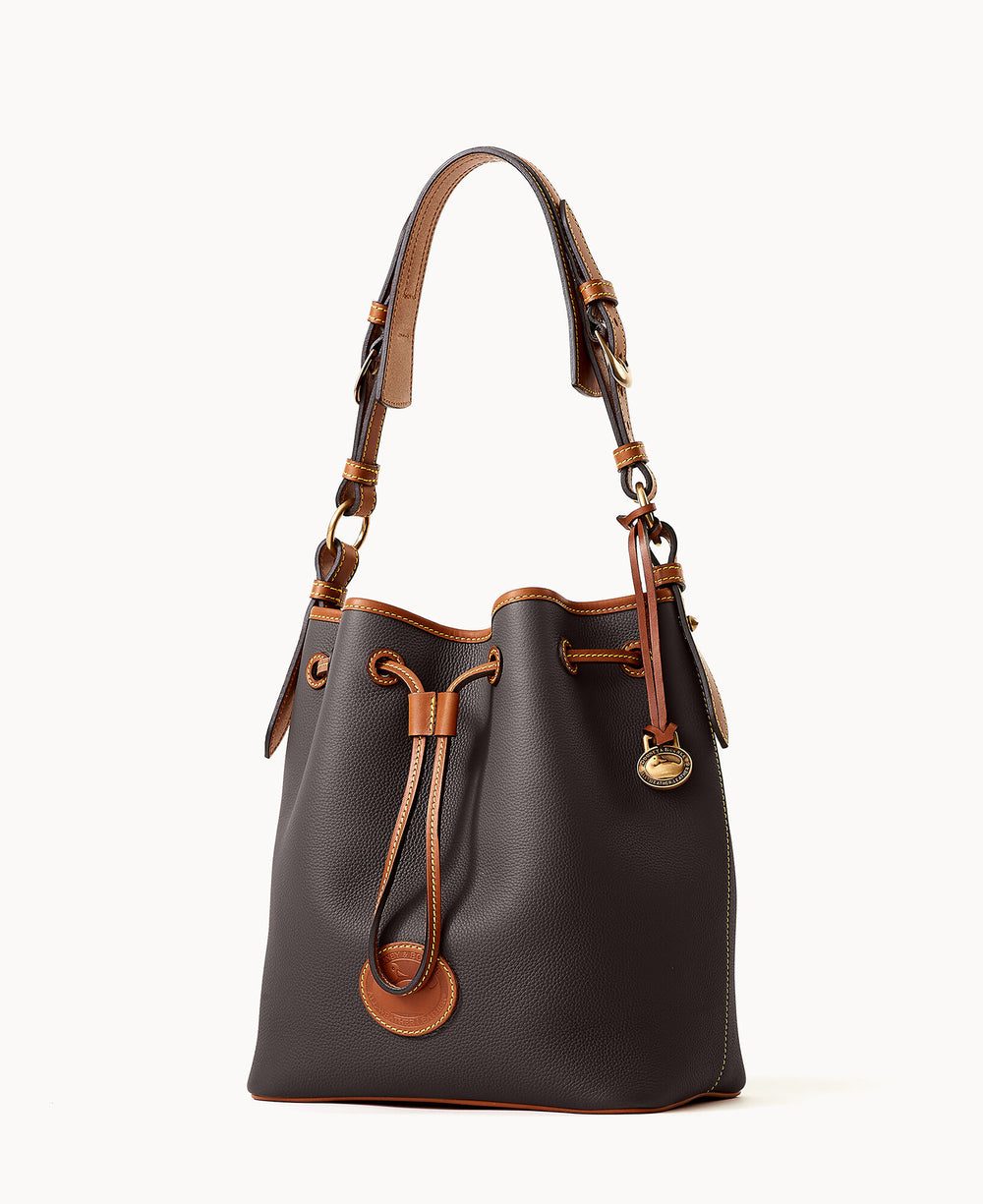 A brown leather bucket bag with tan leather trim, a drawstring closure, gold hardware, and a short shoulder strap. The bag has a structured shape and a decorative logo charm hanging on one side.
