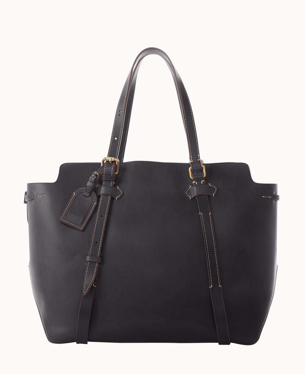 A large black leather tote bag with double handles, decorative belt straps, gold-tone hardware, and a matching luggage tag attached to one handle. The bag features contrast stitching around the edges.