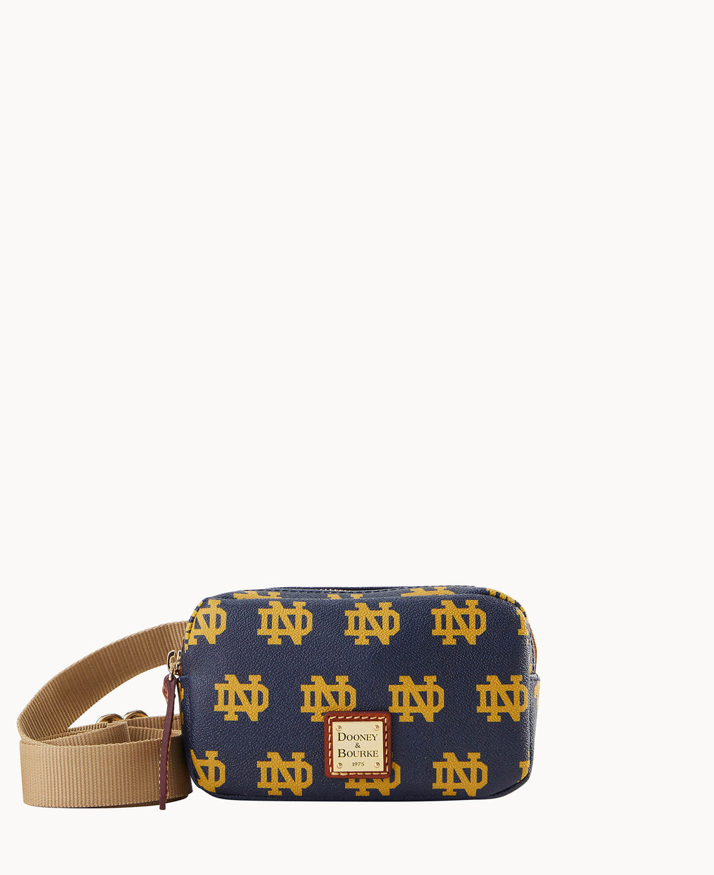 A small navy blue Dooney & Bourke crossbody bag featuring a repeating yellow Notre Dame logo pattern and a beige adjustable strap.
