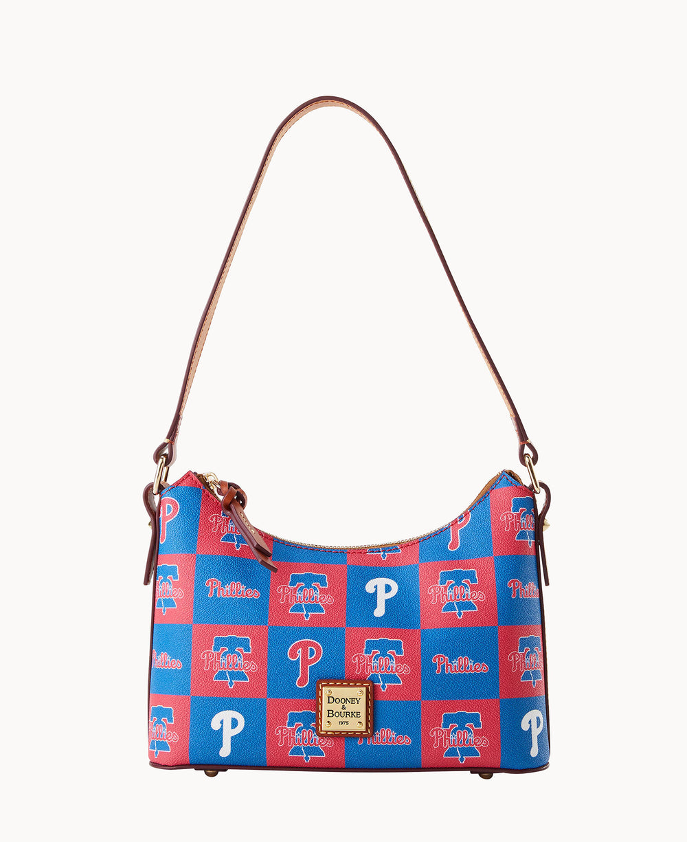 A shoulder bag with a brown strap, featuring a blue and red checkerboard pattern with Philadelphia Phillies logos and text. The bag has a gold Dooney & Bourke label on the front.