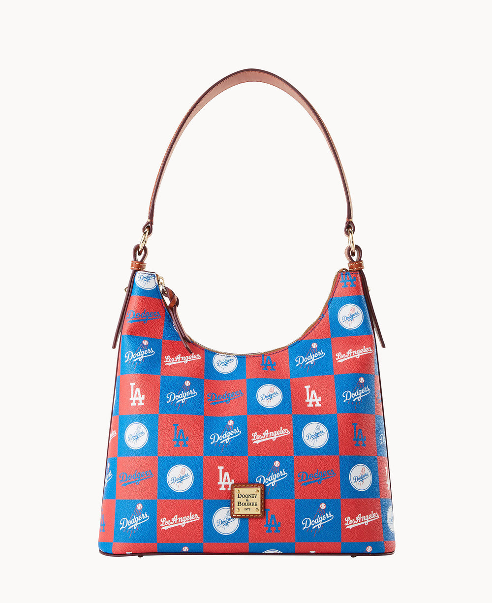 A handbag with a brown strap features a red and blue checkerboard pattern with white Los Angeles Dodgers logos, script, and baseball graphics. A Dooney & Bourke label is on the front.