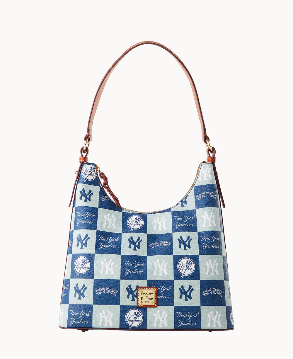 A handbag with a brown strap, featuring a blue and white checkered pattern adorned with various New York Yankees logos and script. A Dooney & Bourke logo patch is on the front.