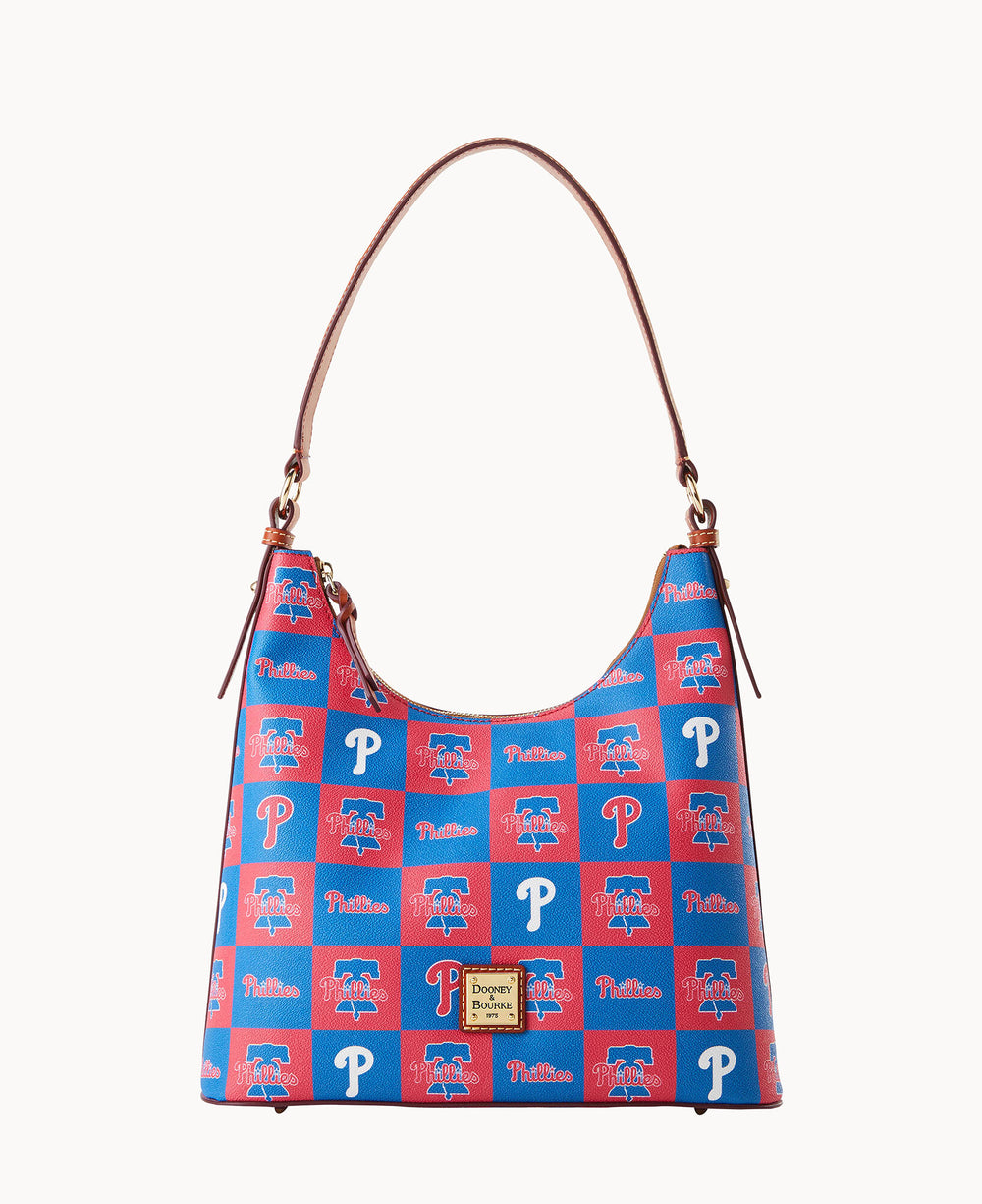 A handbag with a brown leather strap and a blue-and-red checkered pattern featuring the Philadelphia Phillies logo, the Phillies P, and Phillies text, with a gold Dooney & Bourke label on the front.