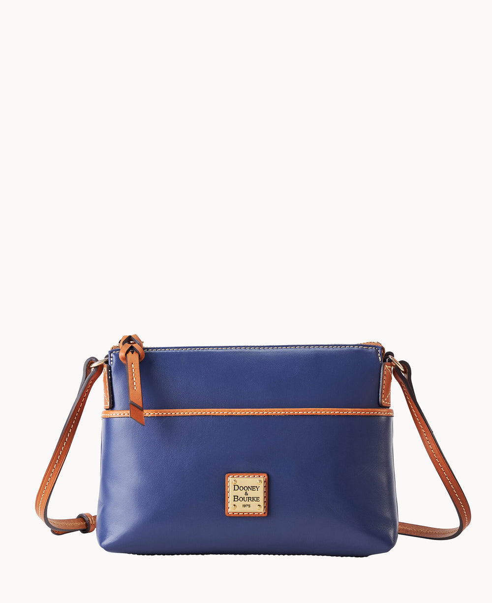 A small blue leather crossbody bag with brown trim and strap, featuring a zip closure and a square Dooney & Bourke logo patch on the front.