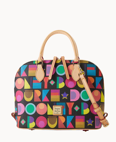 A dome-shaped handbag with tan leather handles and strap, featuring a colorful geometric pattern of circles, squares, and letters on a black background. The front has a small metal Dooney & Bourke logo plate.
